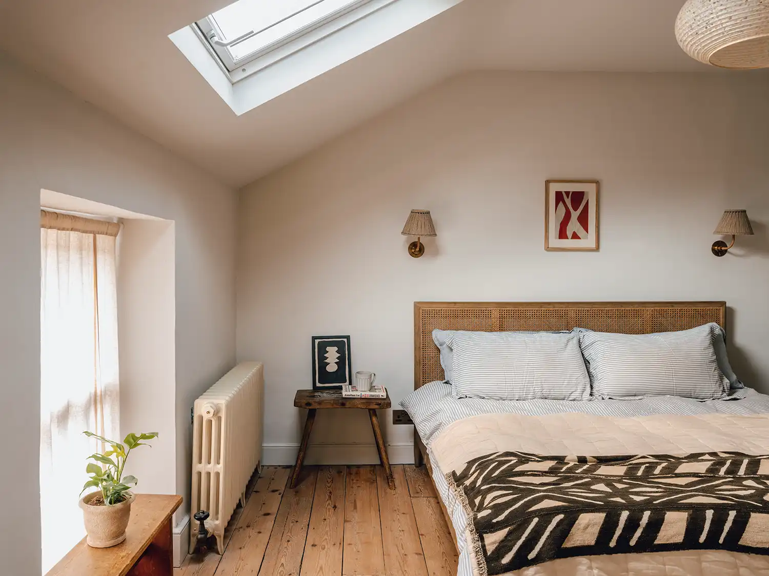 Bedroom with a sloped ceiling, skylight, wooden floors, and a woven headboard.