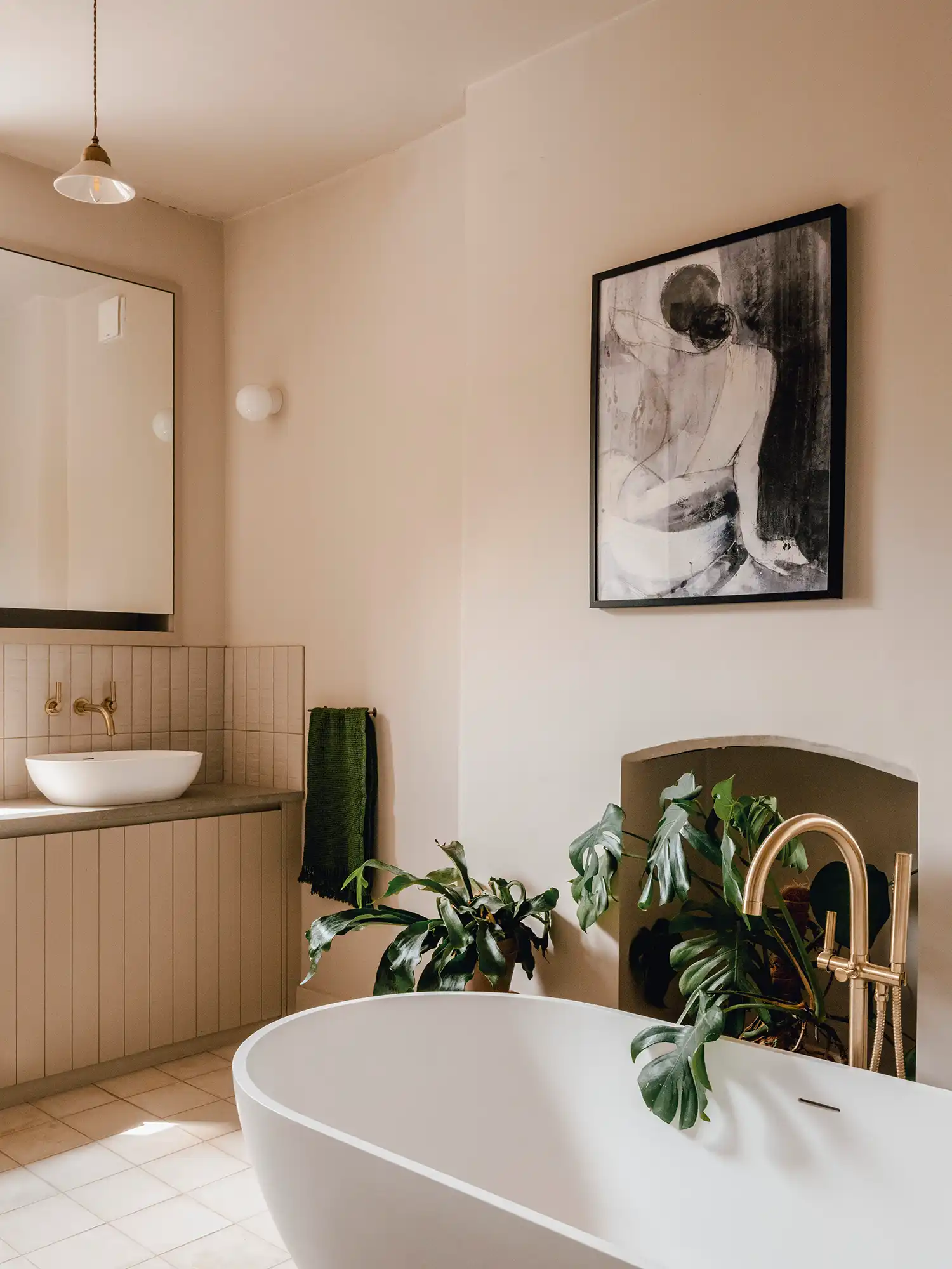 Bathroom with a white freestanding tub, gold fixtures, and a large monstera plant.