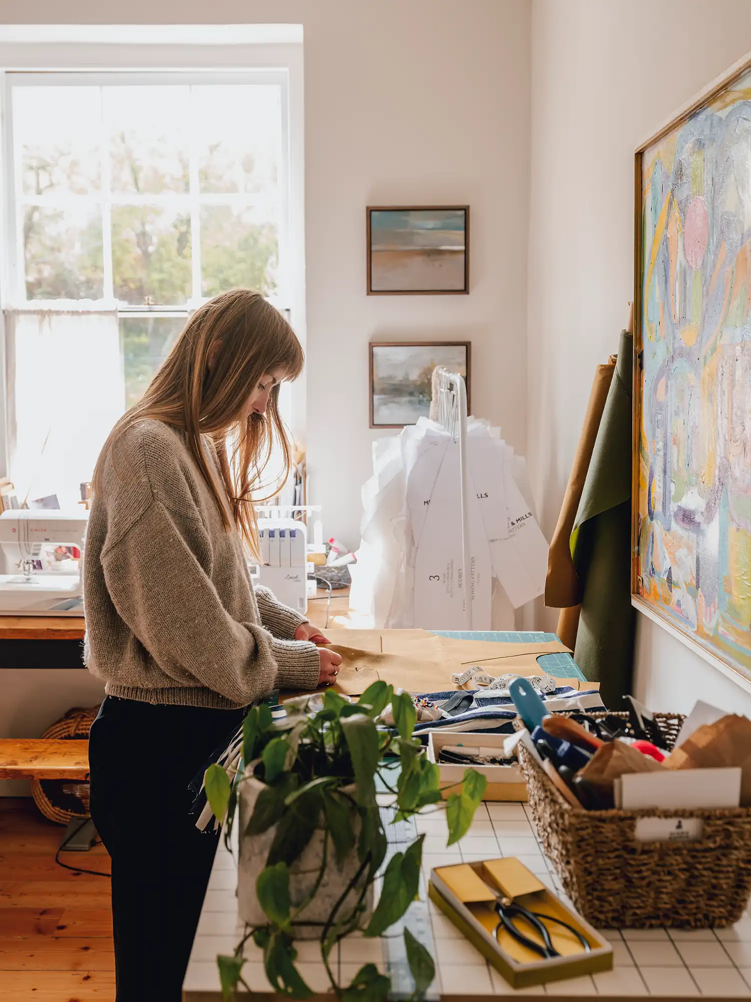 Bright creative studio with a large window, sewing machine, and fabric patterns.