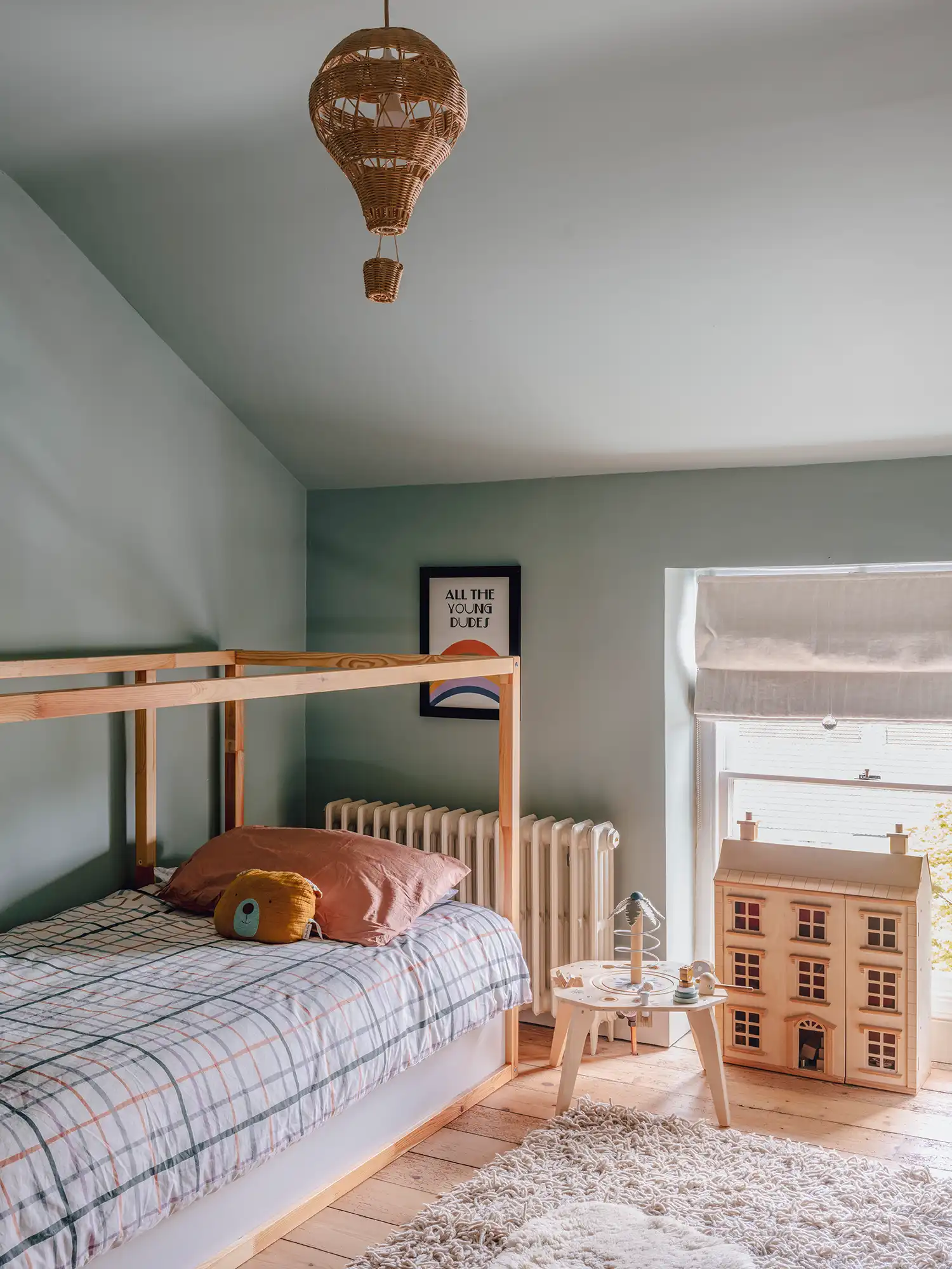 Child’s bedroom with soft green walls, a wooden bed frame, and a dollhouse.