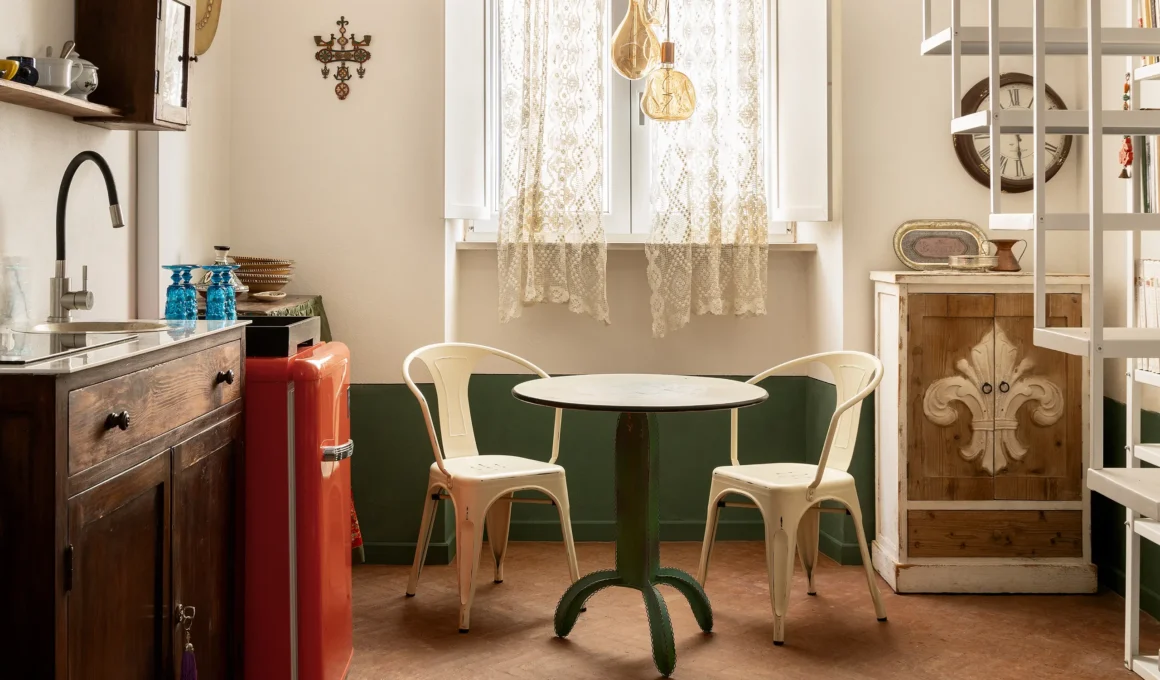 White cafe table and chairs beneath a mezzanine staircase in a high-ceiling Caserta apartment.