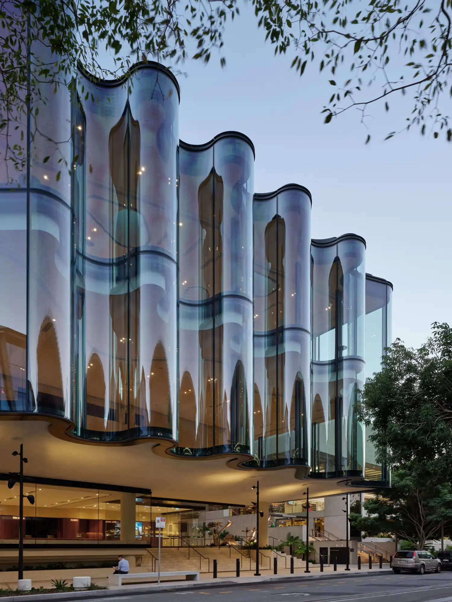 Low-angle view of the rippling glass façade showing reflections of trees and sky.