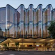 Close-up of the rippling glass façade of the Glasshouse Theatre in Brisbane against a clear sky.
