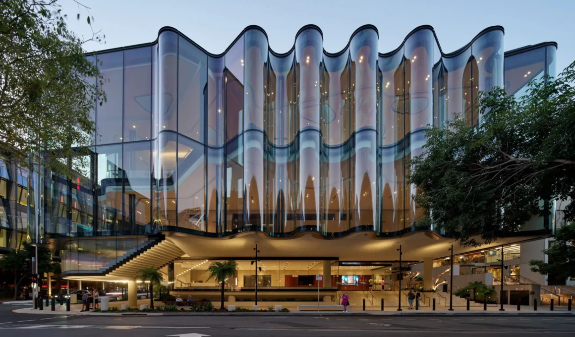 Close-up of the rippling glass façade of the Glasshouse Theatre in Brisbane against a clear sky.