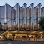 Close-up of the rippling glass façade of the Glasshouse Theatre in Brisbane against a clear sky.