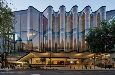 Close-up of the rippling glass façade of the Glasshouse Theatre in Brisbane against a clear sky.