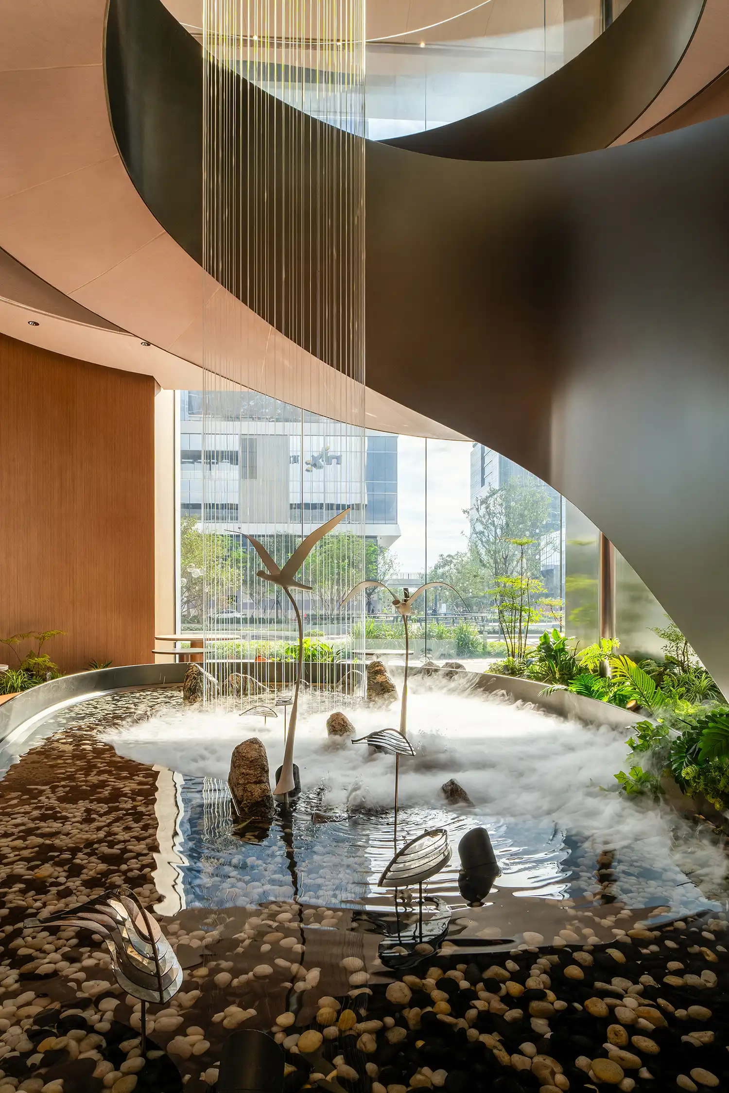 Internal water feature with decorative birds, mist, and cascading strings inside a spiral staircase