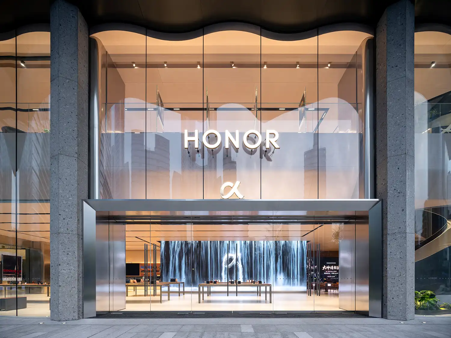 Main entrance to the HONOR flagship store with large illuminated logos and an interior digital waterfall