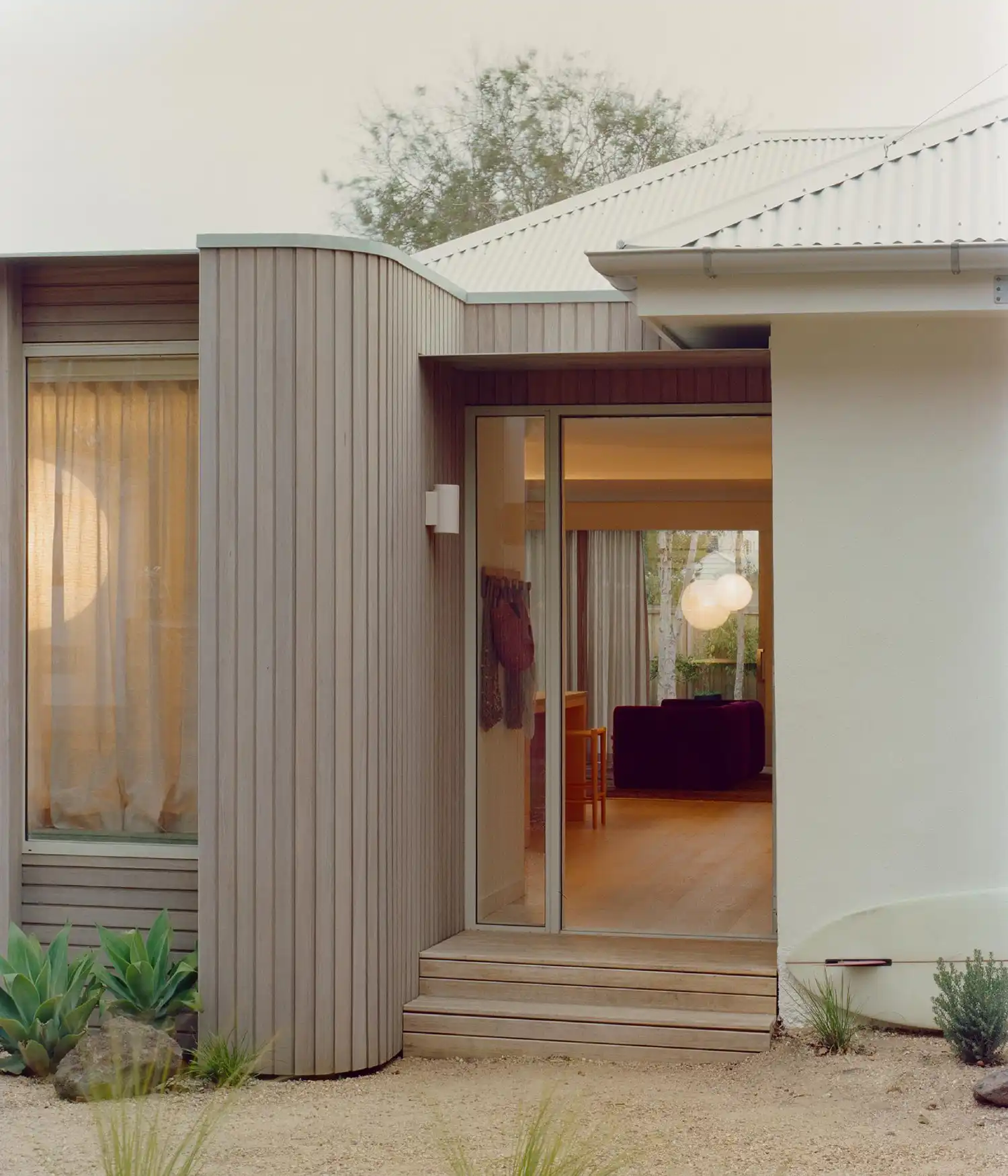 Close-up of a curved timber wall and glass entryway at dusk.