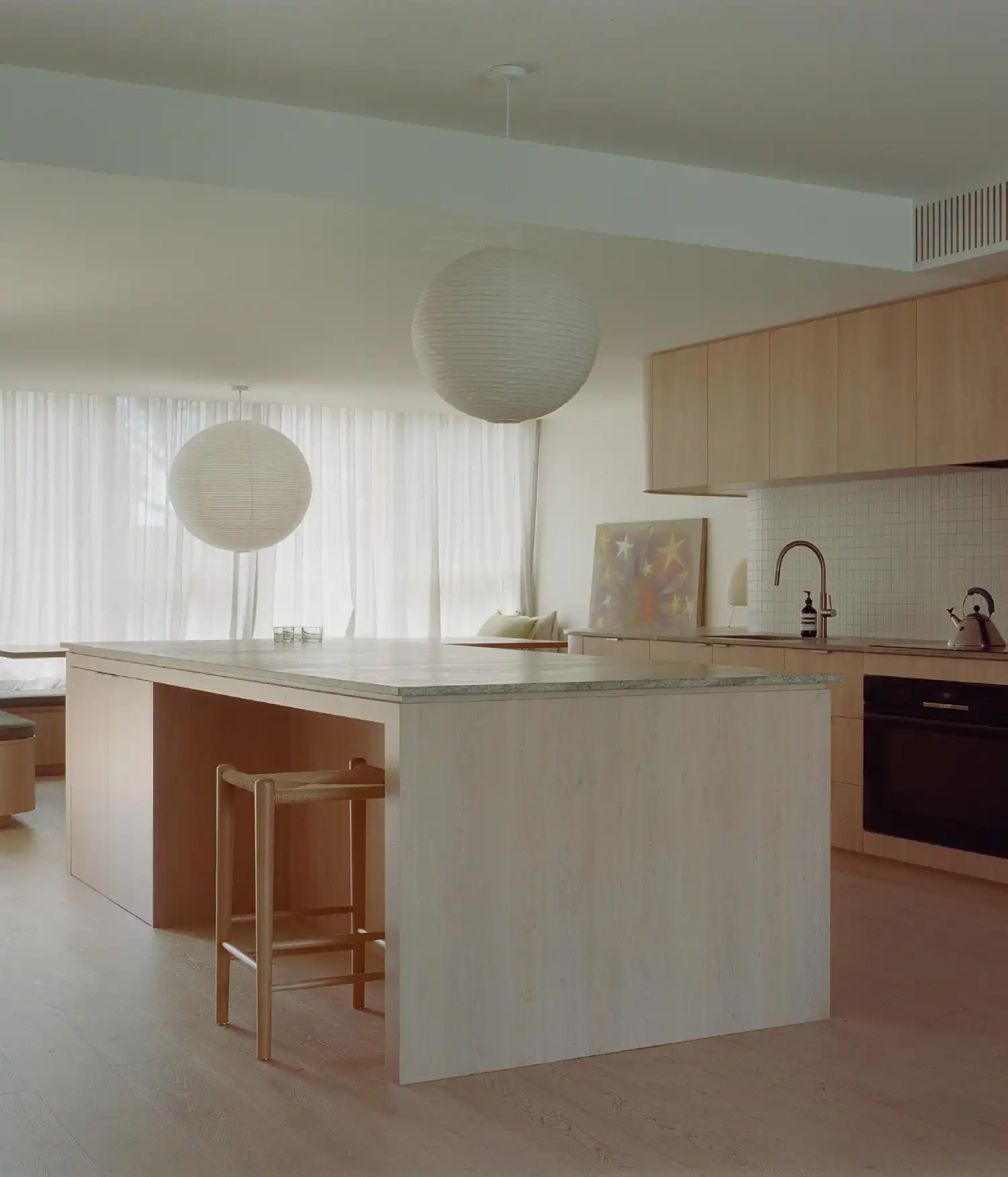 Modern kitchen with a large wooden island and paper lantern pendants.