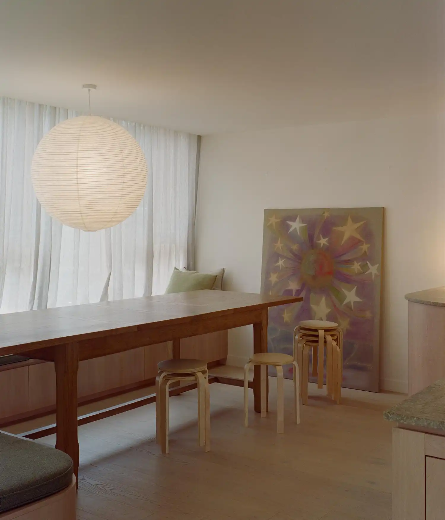 Dining area with a long wooden table, stackable stools, and a large paper pendant.