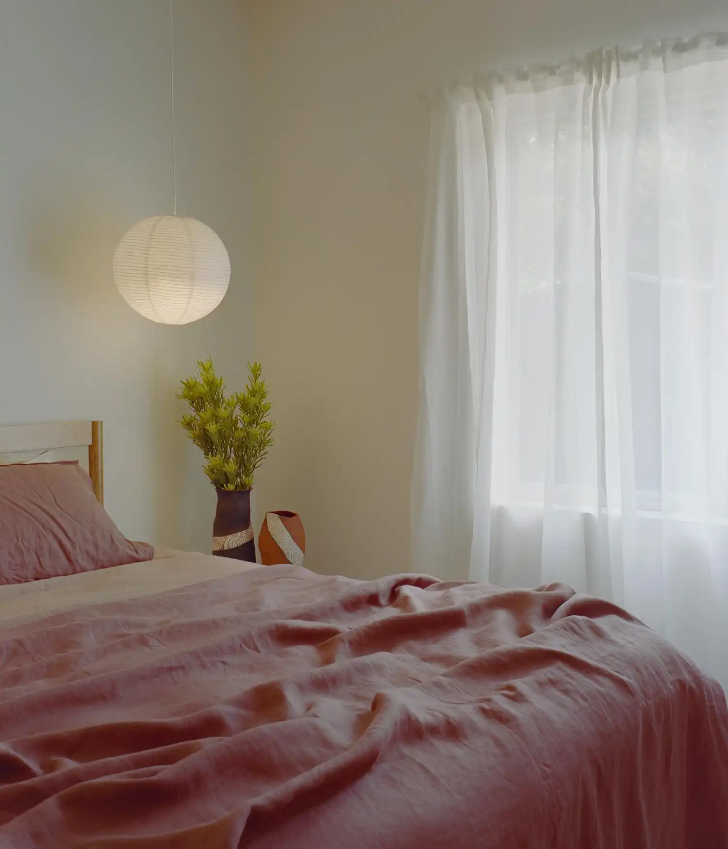 Bedroom with soft pink linen bedding and a paper lantern light.