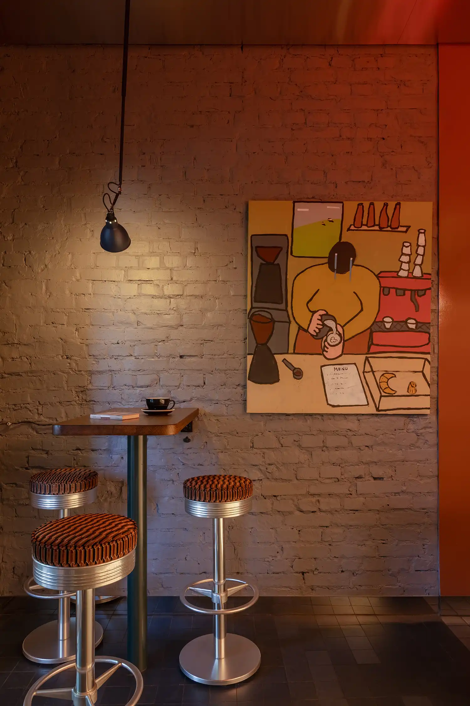 Compact seating area with vintage metal bar stools and modern art on a grey brick wall.
