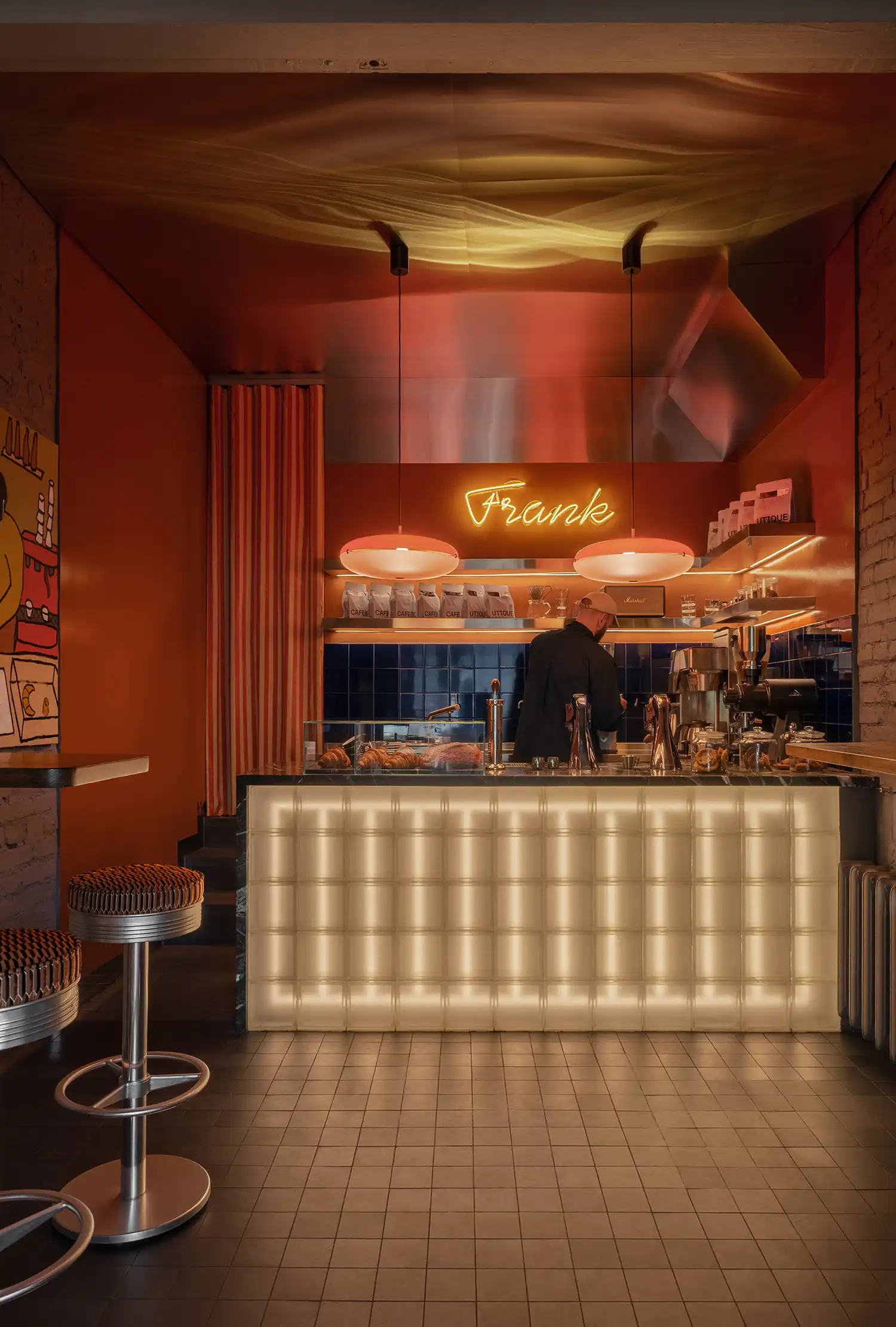 Barista working behind a stainless steel counter with glowing "Frank" neon sign.