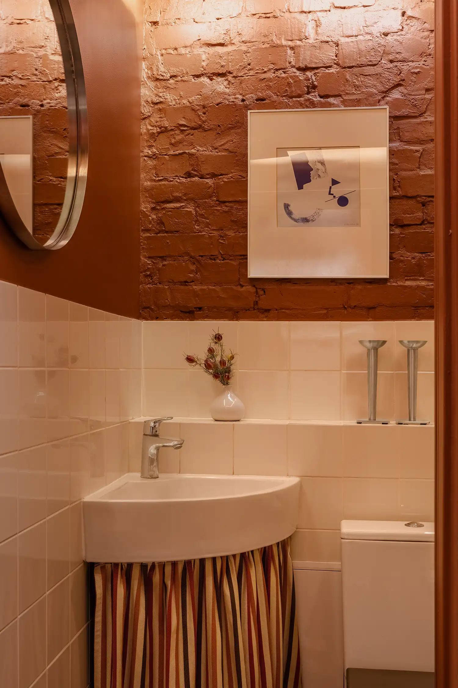 Bathroom interior with terracotta brick walls, white tiles, and striped fabric skirt.