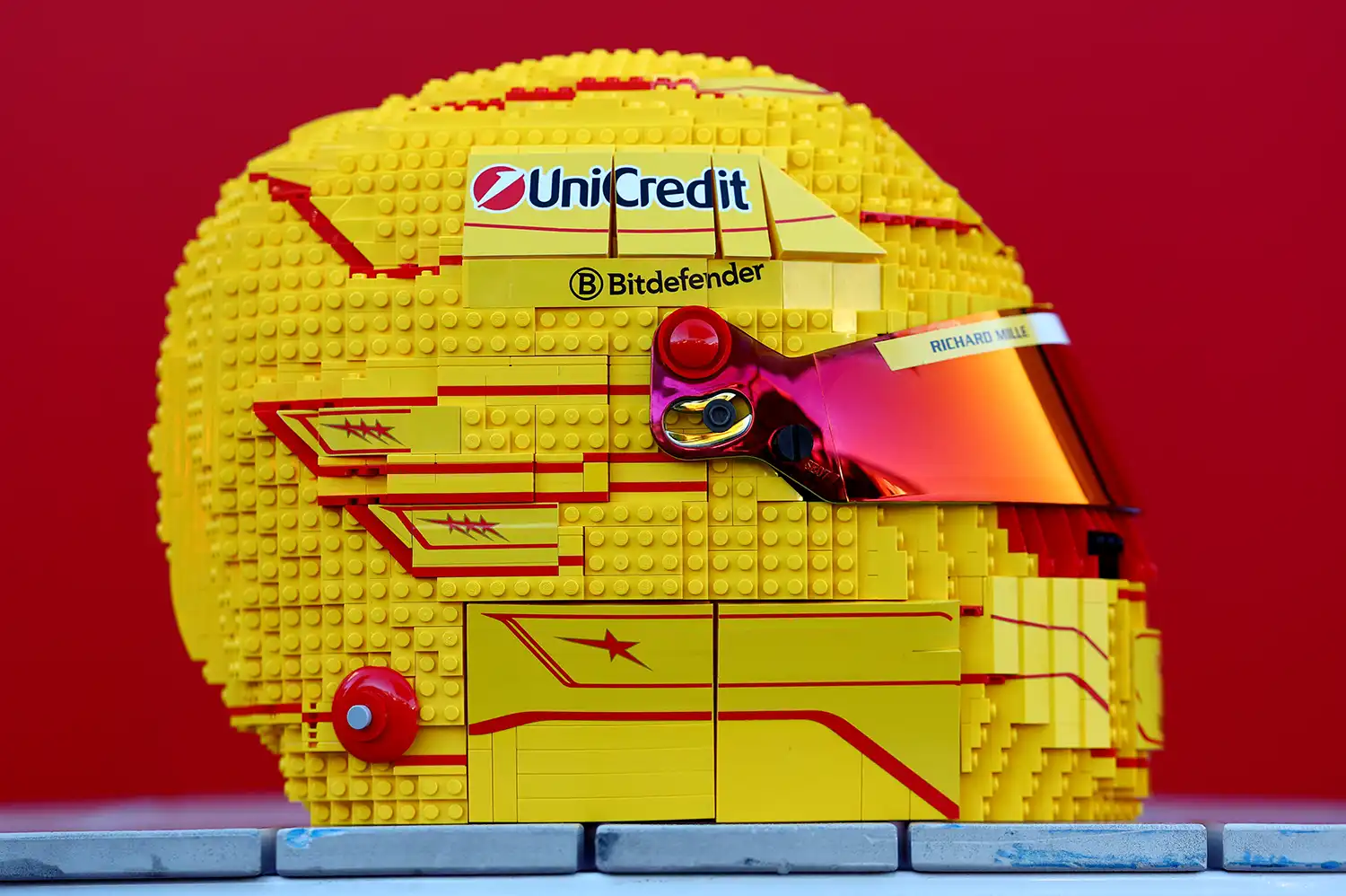 Side profile of a yellow life-sized LEGO Ferrari helmet with UniCredit and Bitdefender logos.