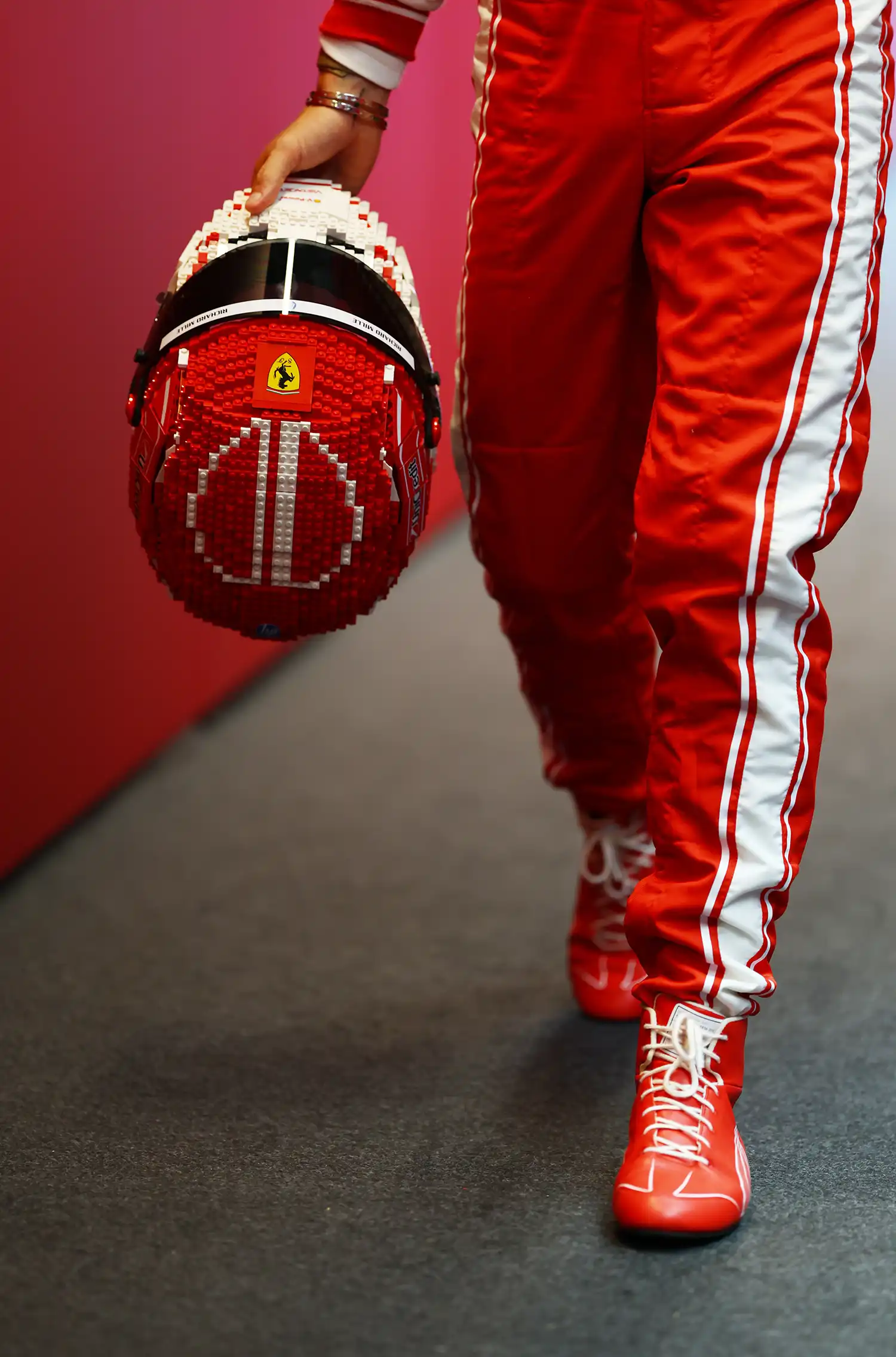 Close-up of Charles Leclerc's hands holding the red and white LEGO helmet while walking.