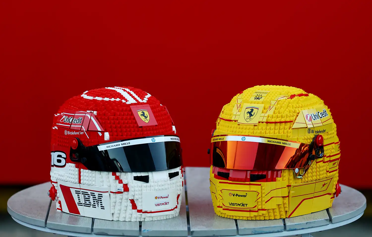 Two life-sized LEGO Ferrari helmets, one red and white, one yellow, sitting side-by-side.