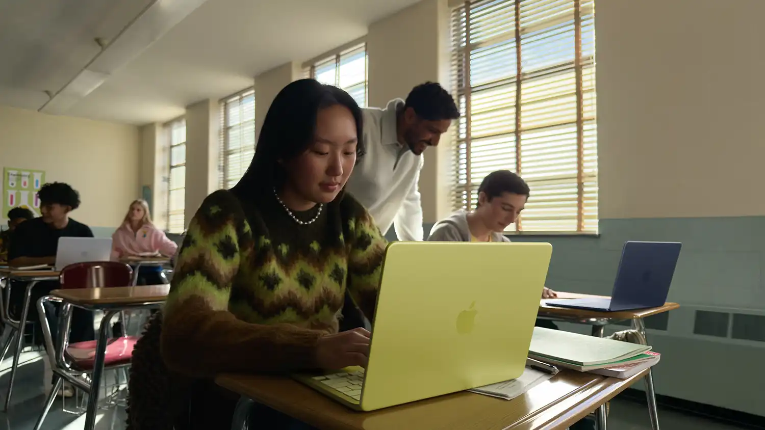 Student using a citrus MacBook Neo in a classroom setting.