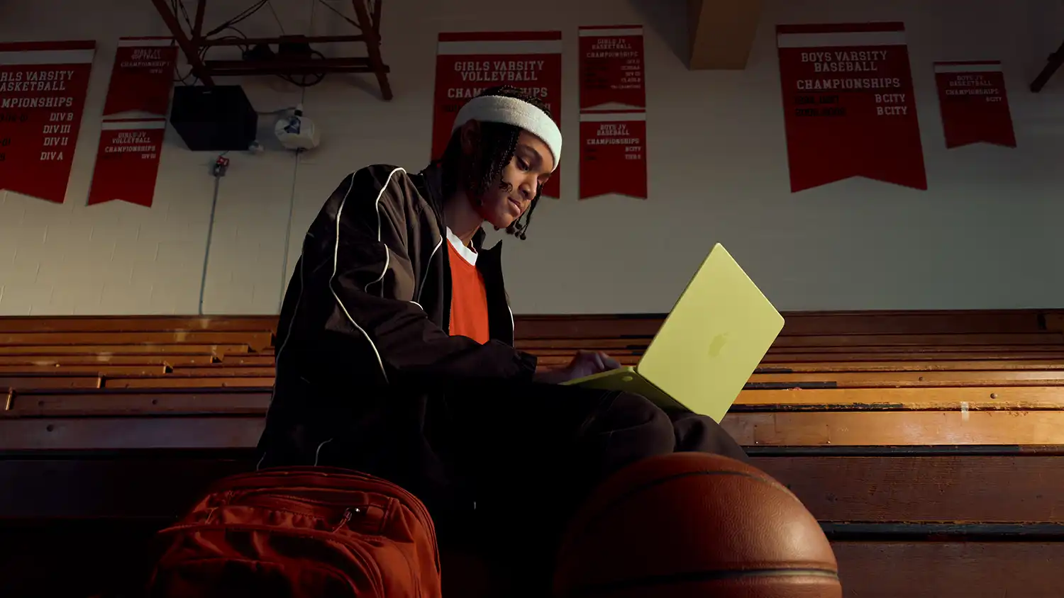 A student using a citrus MacBook Neo on gymnasium bleachers.