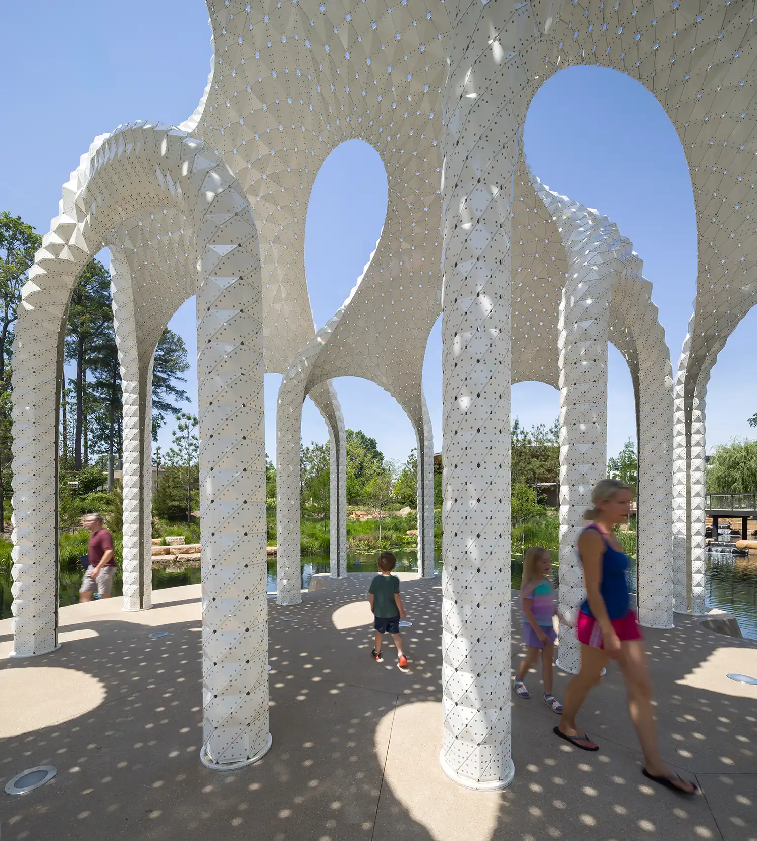 Interior view of L’île Folie pavilion showing dappled light patterns and people walking through.