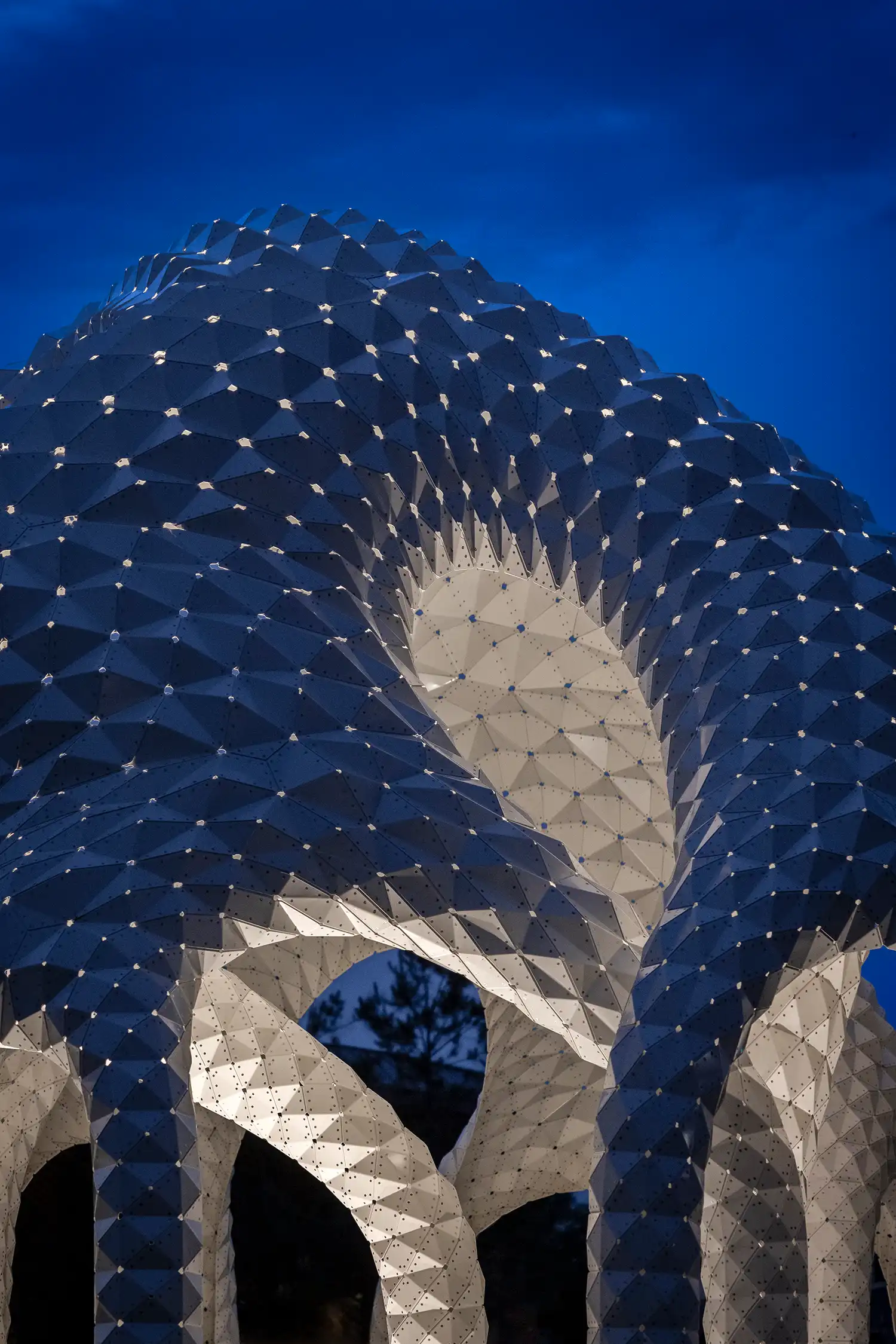 Night photography of L’île Folie pavilion illuminated from within against a dark blue sky.
