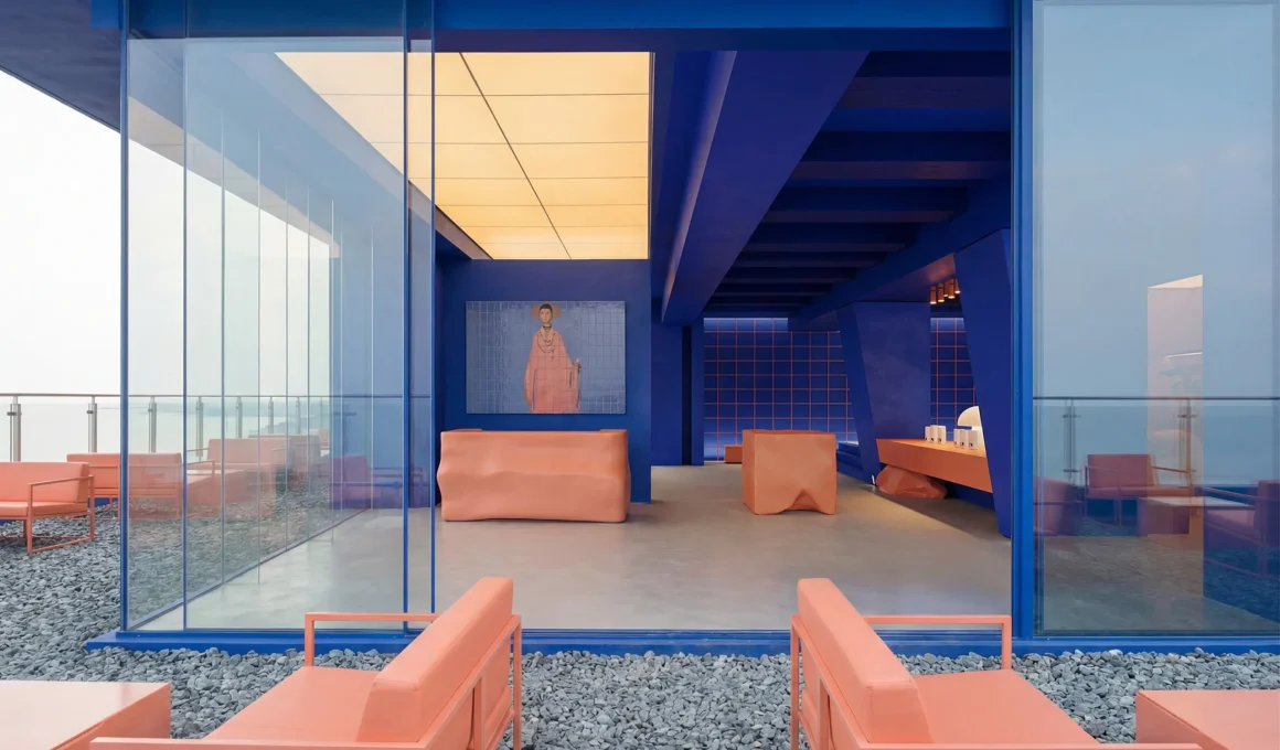 Wide view of BLUO Cafe interior and terrace featuring deep blue architectural elements and terracotta furniture overlooking the sea.