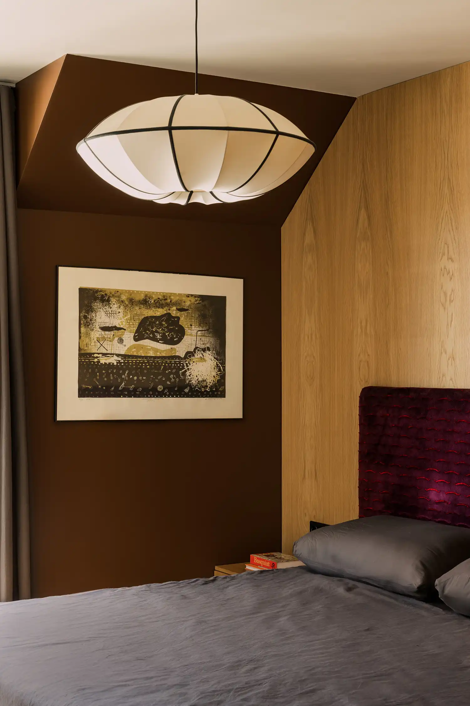 Moody bedroom interior with chocolate brown walls, oak headboard, and silk OiSoOi pendant lamp.