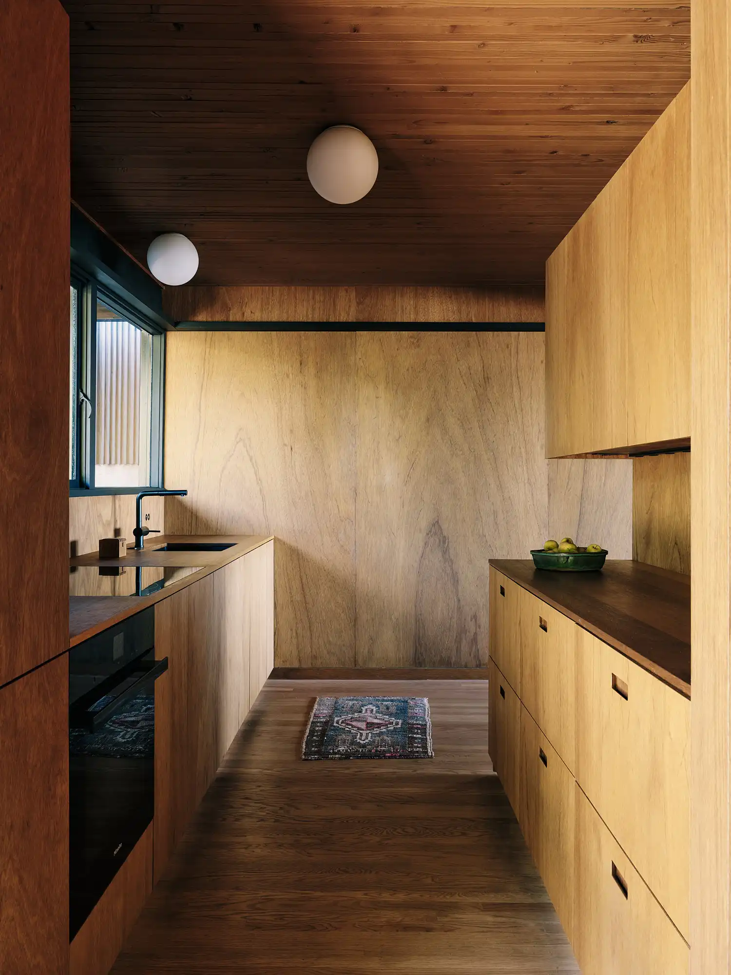 Minimalist galley kitchen with wooden cabinetry, integrated appliances, and red oak flooring.