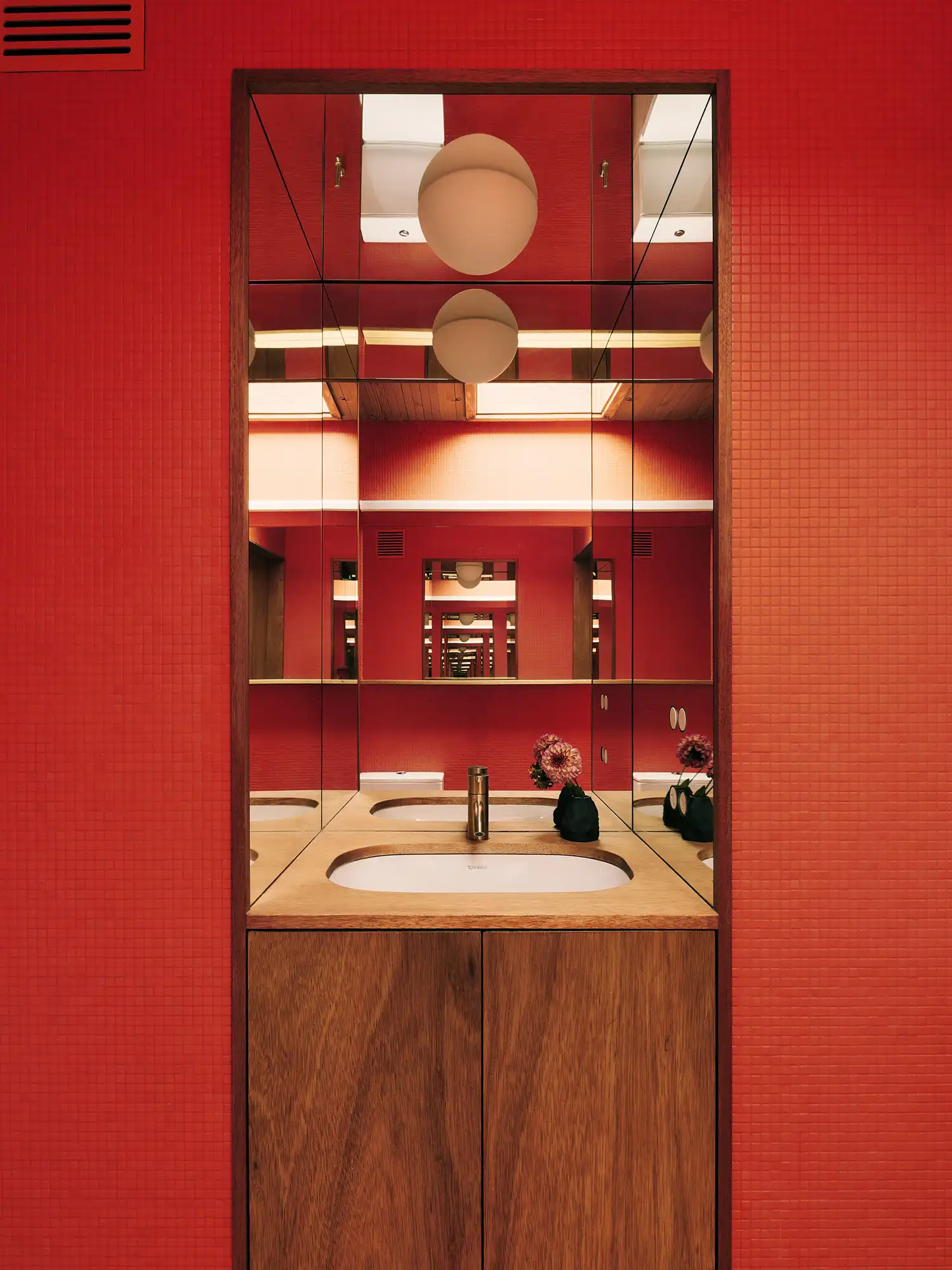 Bathroom interior with vibrant red mosaic tiles and a mirror reflecting the room's geometry.