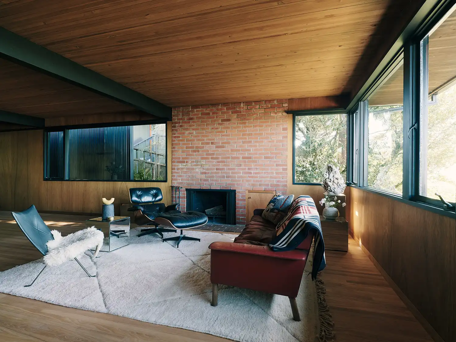 Mid-century living room with brick fireplace, Eames Lounge Chair, and large ribbon windows.
