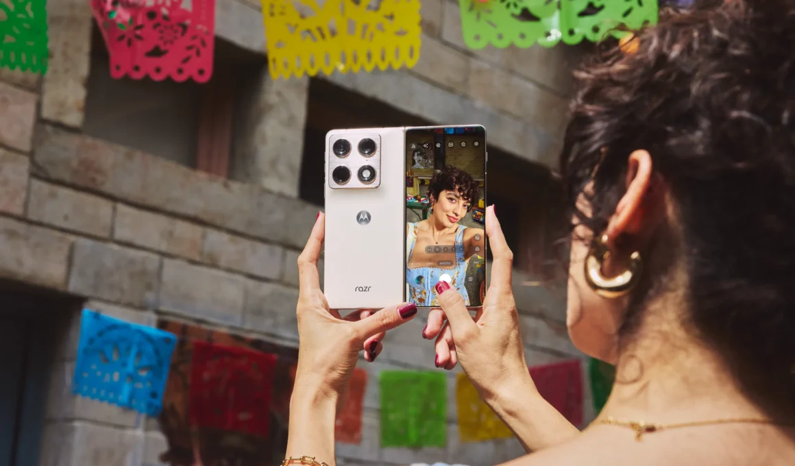 Person taking a selfie with an open white motorola razr fold smartphone, showing the rear camera module and interior screen viewfinder.