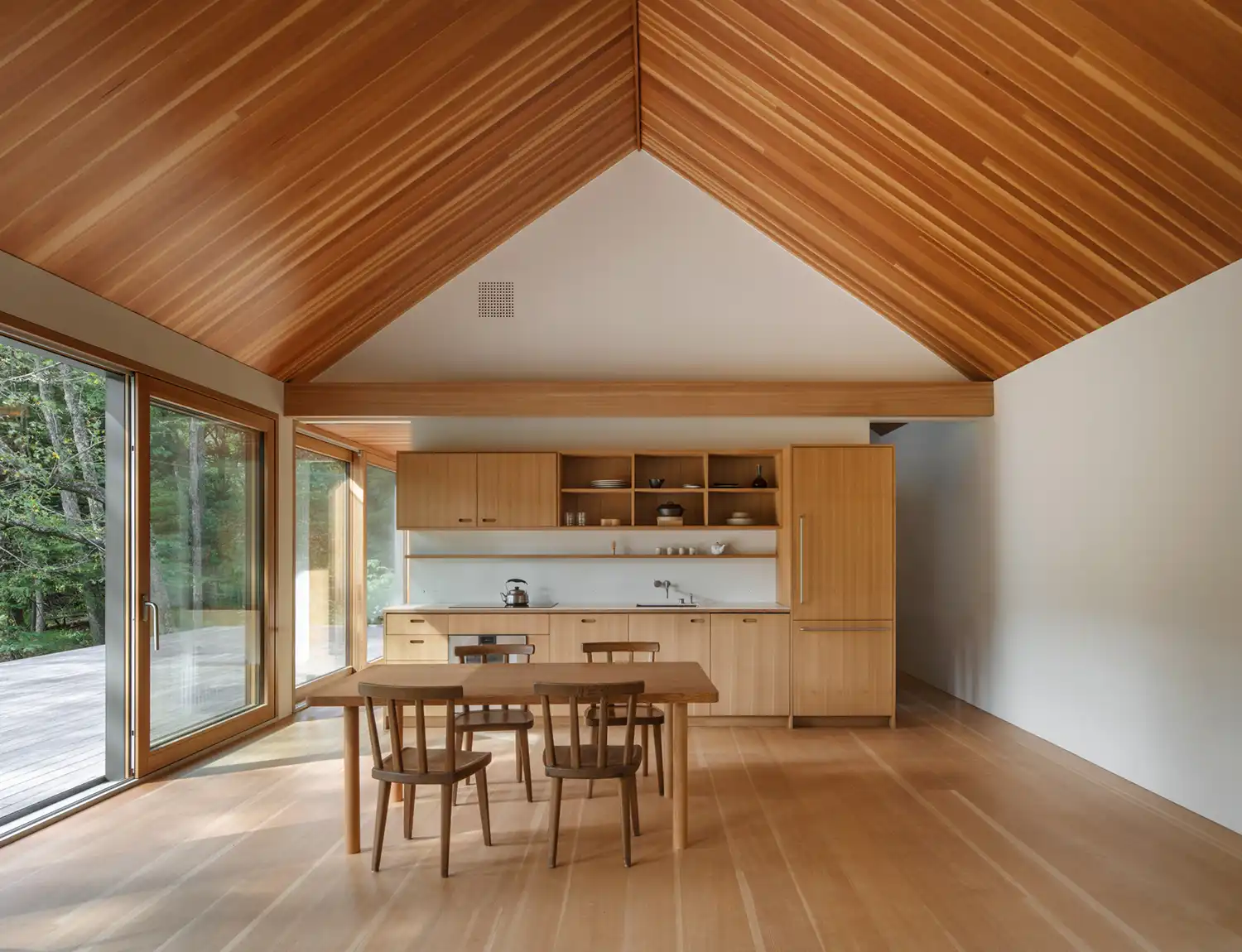 Interior of a kitchen and dining area with a pitched wood-lined ceiling and fir cabinetry.