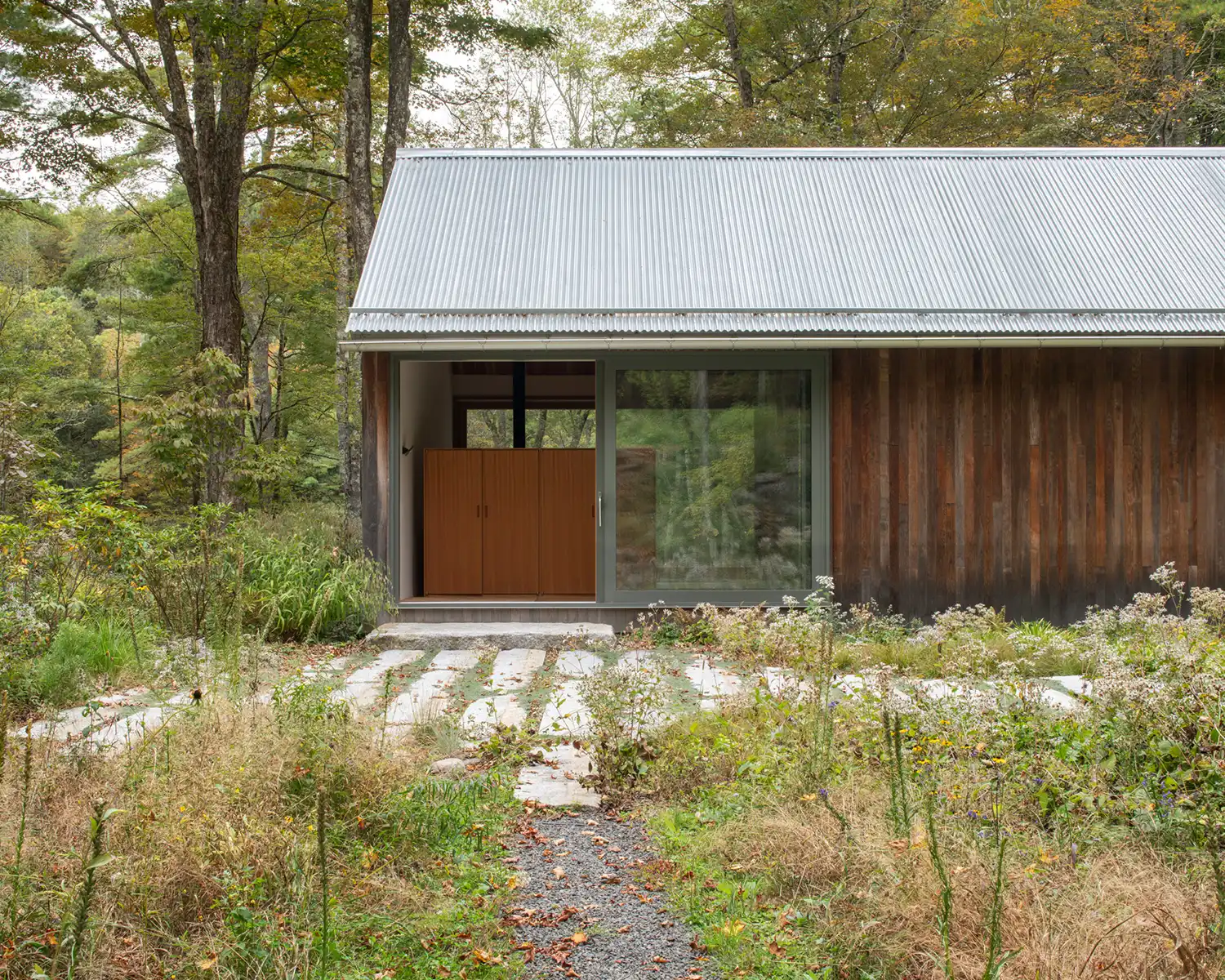 Detailed view of a sliding glass entry door and vertical wood facade near a stone path.