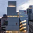 Exterior of OMA’s prismatic New Museum extension at dusk with glowing interior circulation.