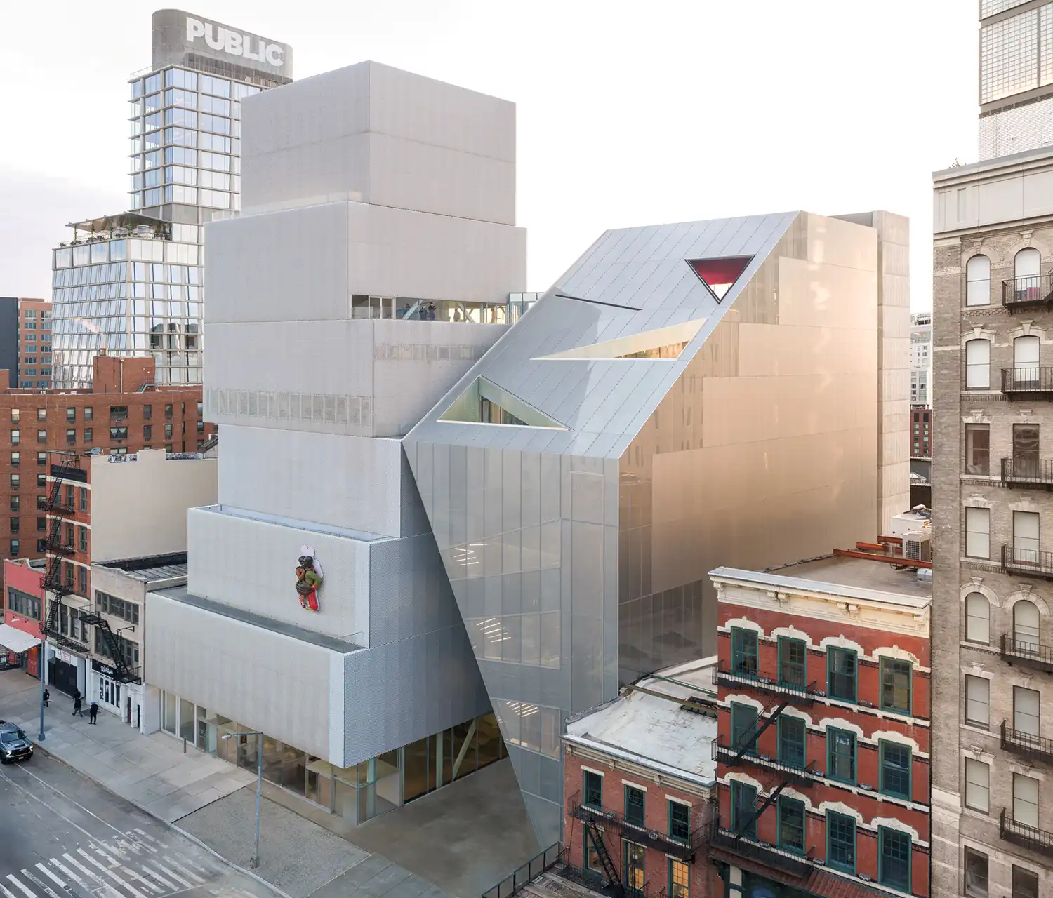 Daytime aerial view of OMA’s metallic mesh extension "kissing" the SANAA building.
