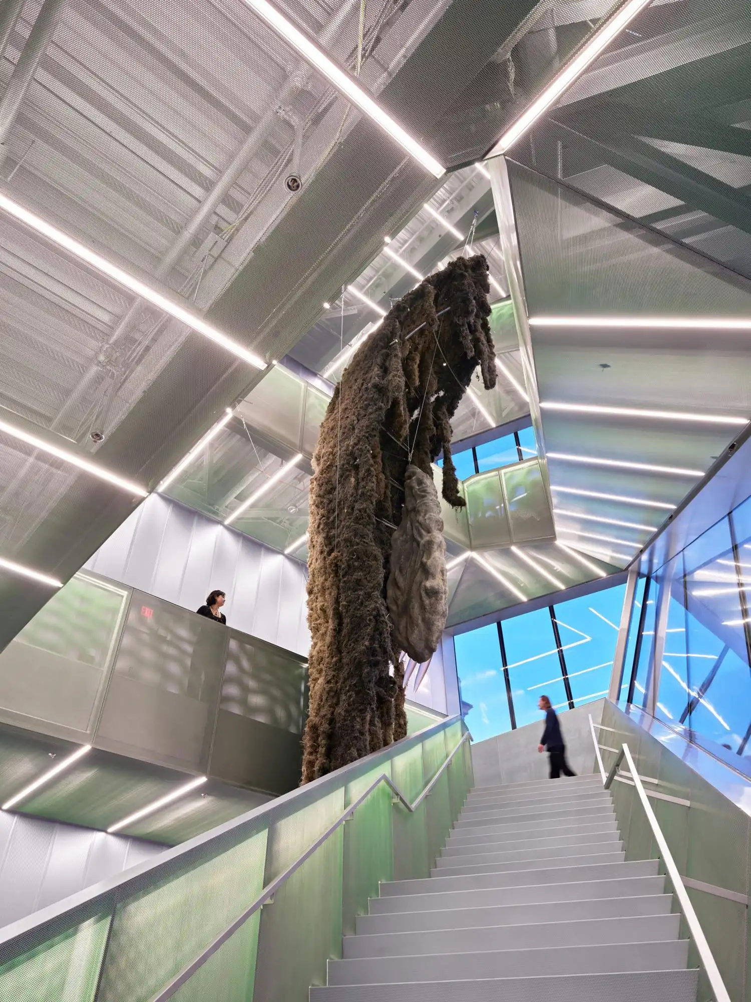 Interior of the OMA New Museum atrium featuring a tall, organic sculpture and mesh stairs.