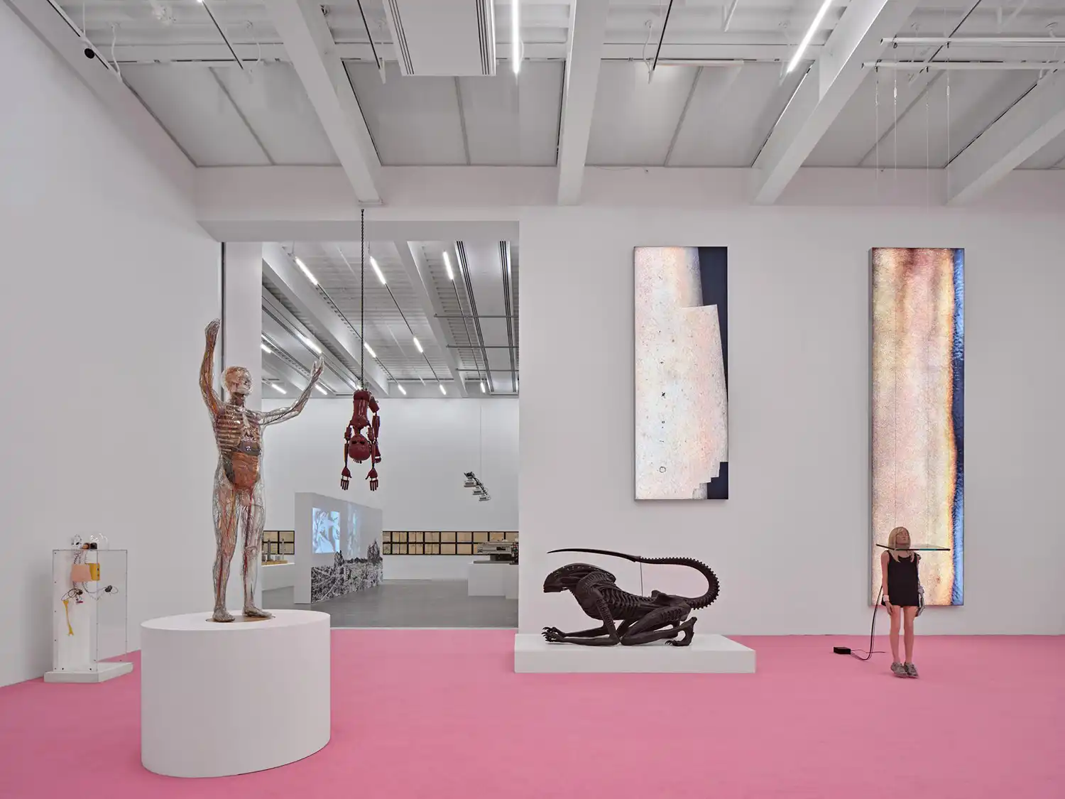 Minimalist white gallery space with pink flooring and diverse contemporary sculptures.