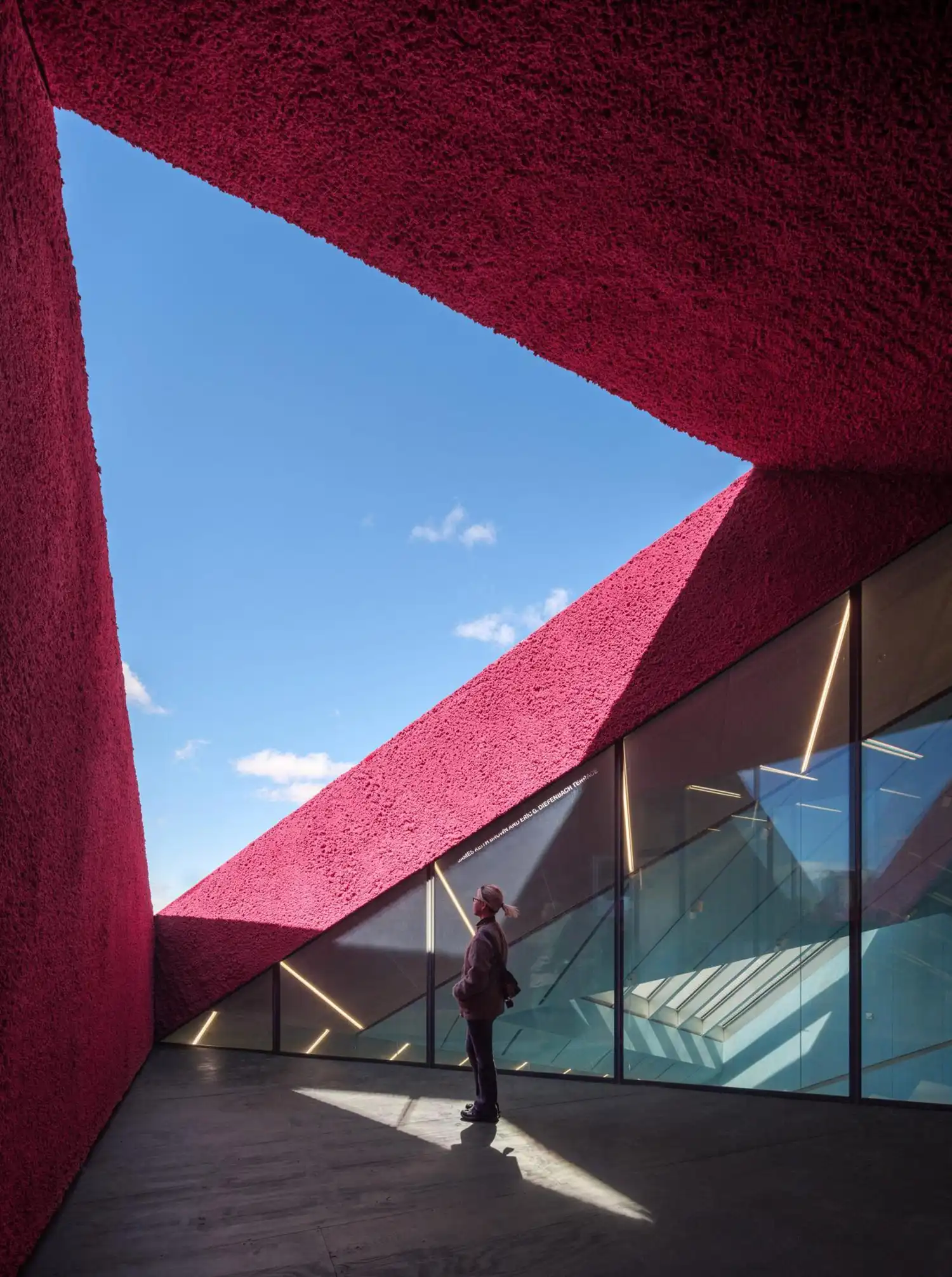 Outdoor balcony with textured red walls and views through the angular building skin.