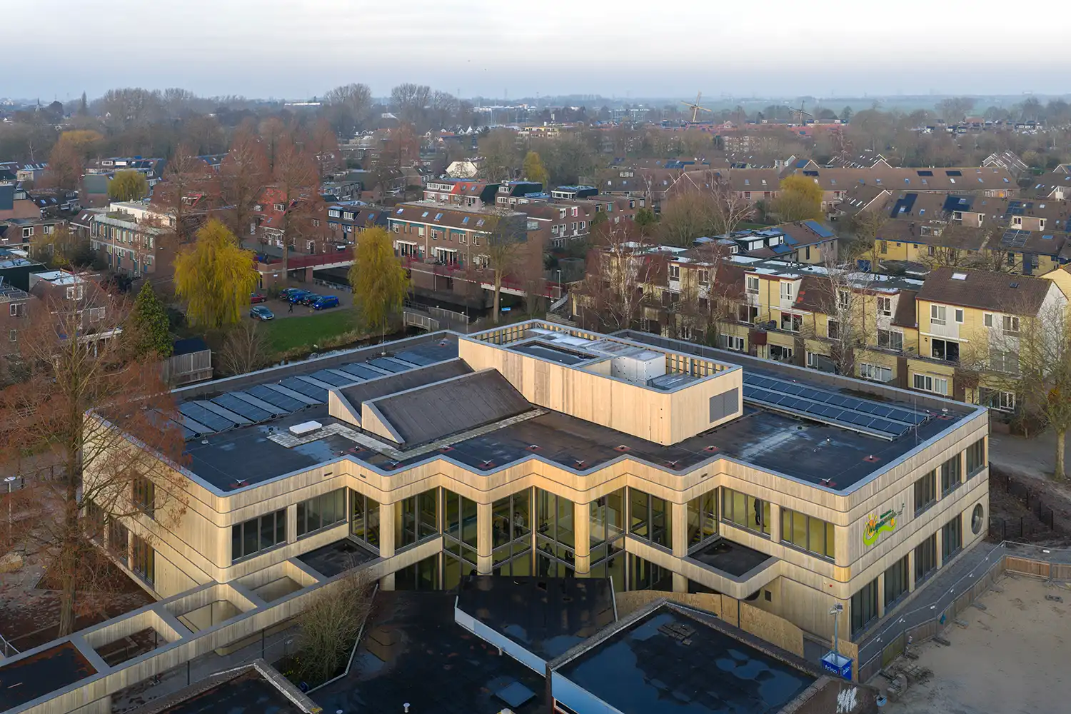 Aerial view of the compact Wisperweide school in Amsterdam, showing the textured timber facade and extensive rooftop solar panels.