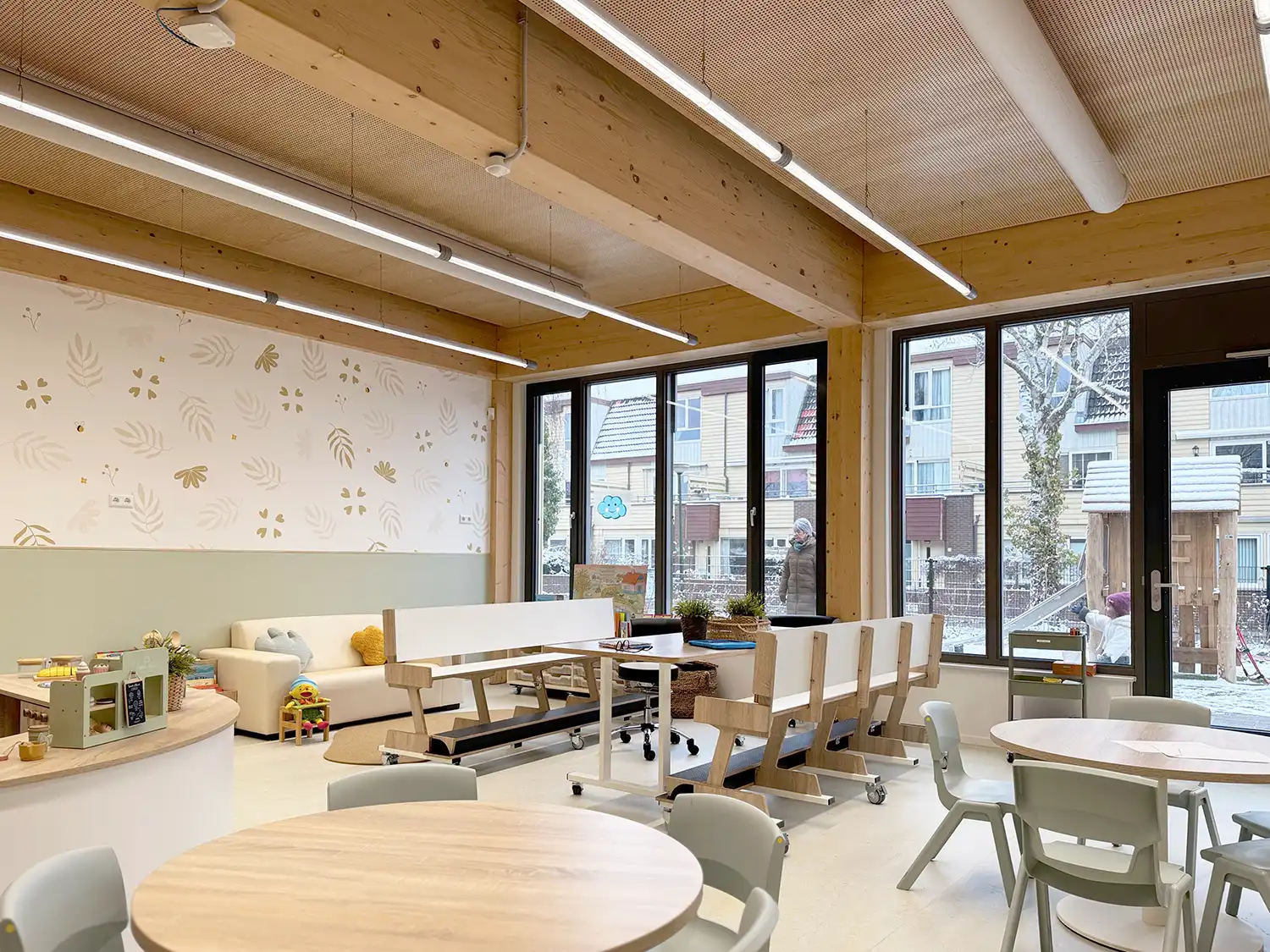 A flexible classroom with transparent internal walls, ergonomic wooden furniture, and wide windows overlooking an Amsterdam neighborhood.