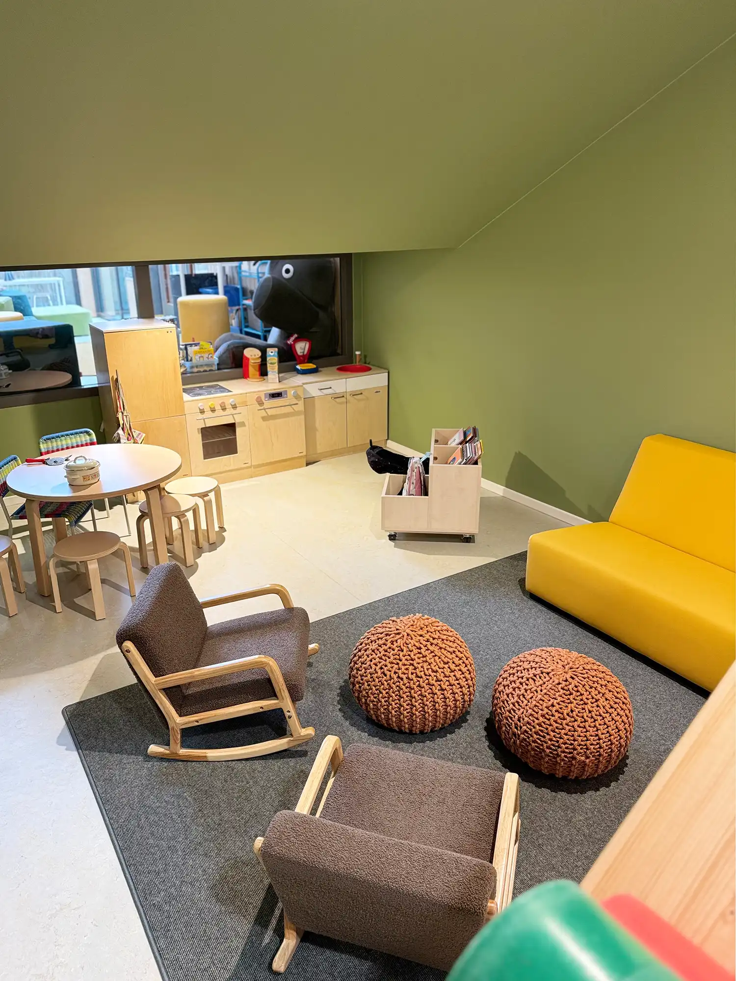 A focused view of a sensory-rich reading corner with colorful library bins, plush woven ottomans, and warm, textured wood flooring.