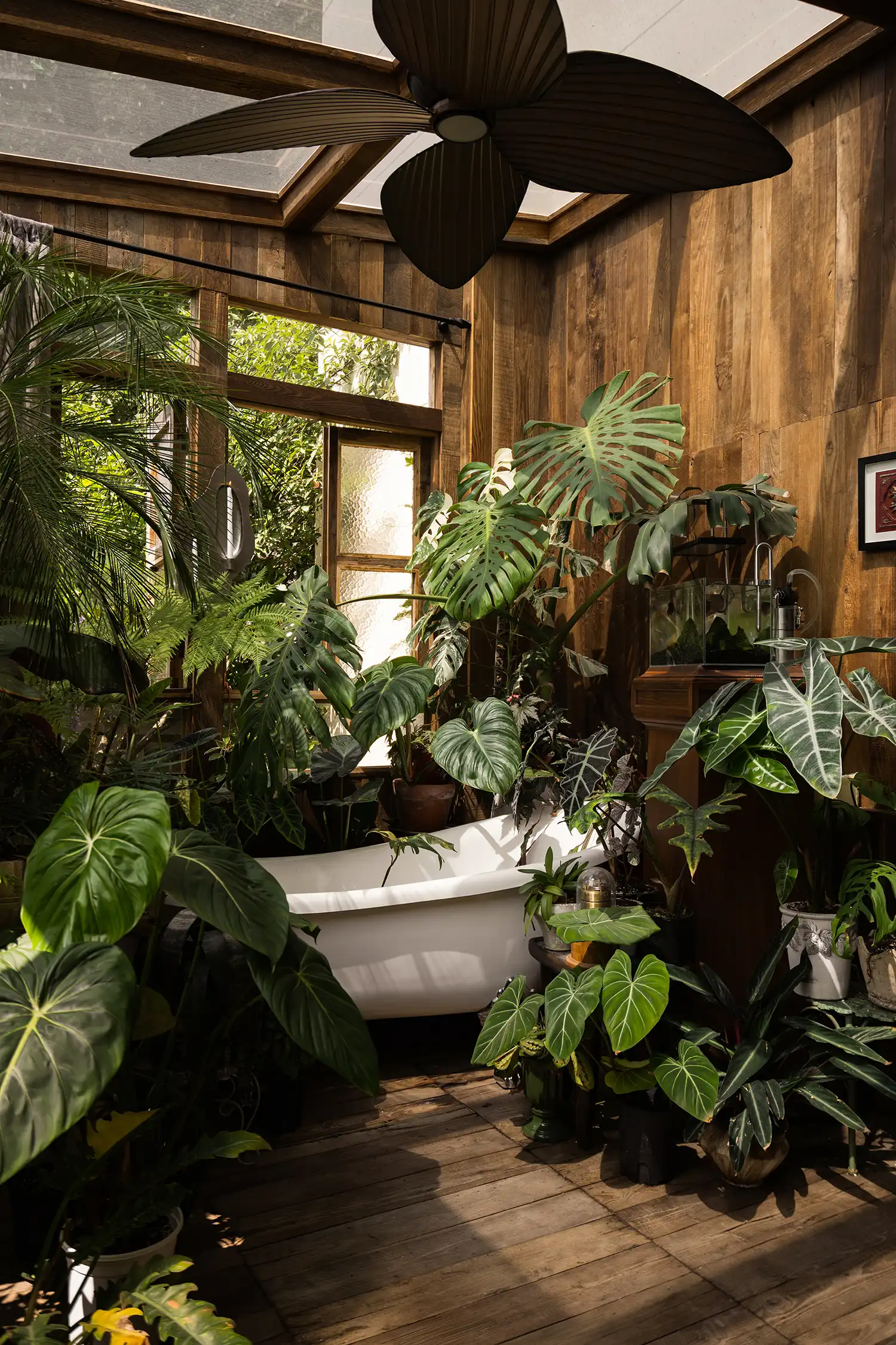 A bathtub is nestled within the greenery of the small timber cabin, placed near a free-spirited study.