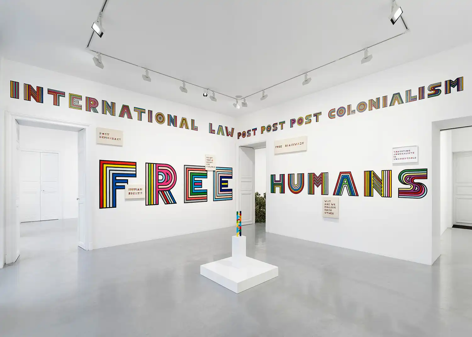 Large-scale colorful typographic embroidery on gallery walls with words like FREE, HUMANS, and INTERNATIONAL LAW.