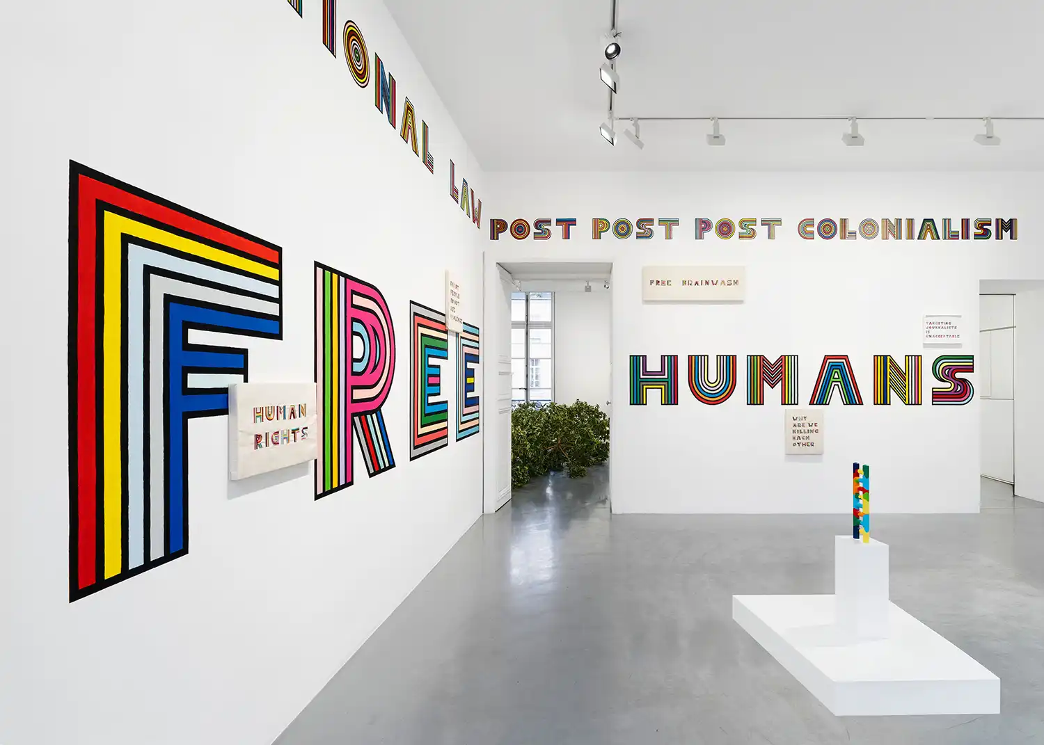 Close-up of the "FREE" and "HUMANS" silk embroidery showing the intricate rainbow-striped thread patterns.