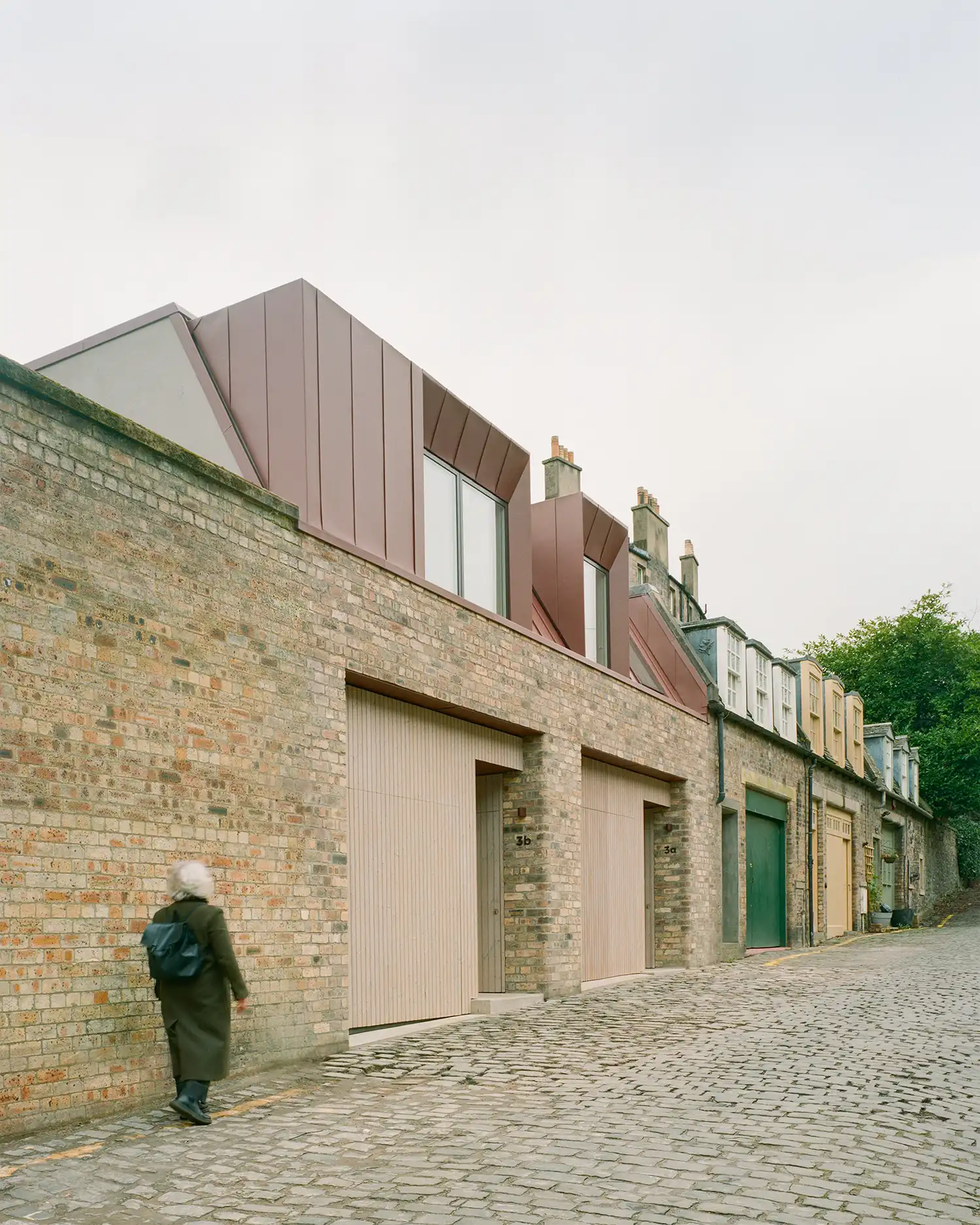 Reclaimed brick facade of Canon Mews with red zinc upper story on a cobbled Edinburgh street.