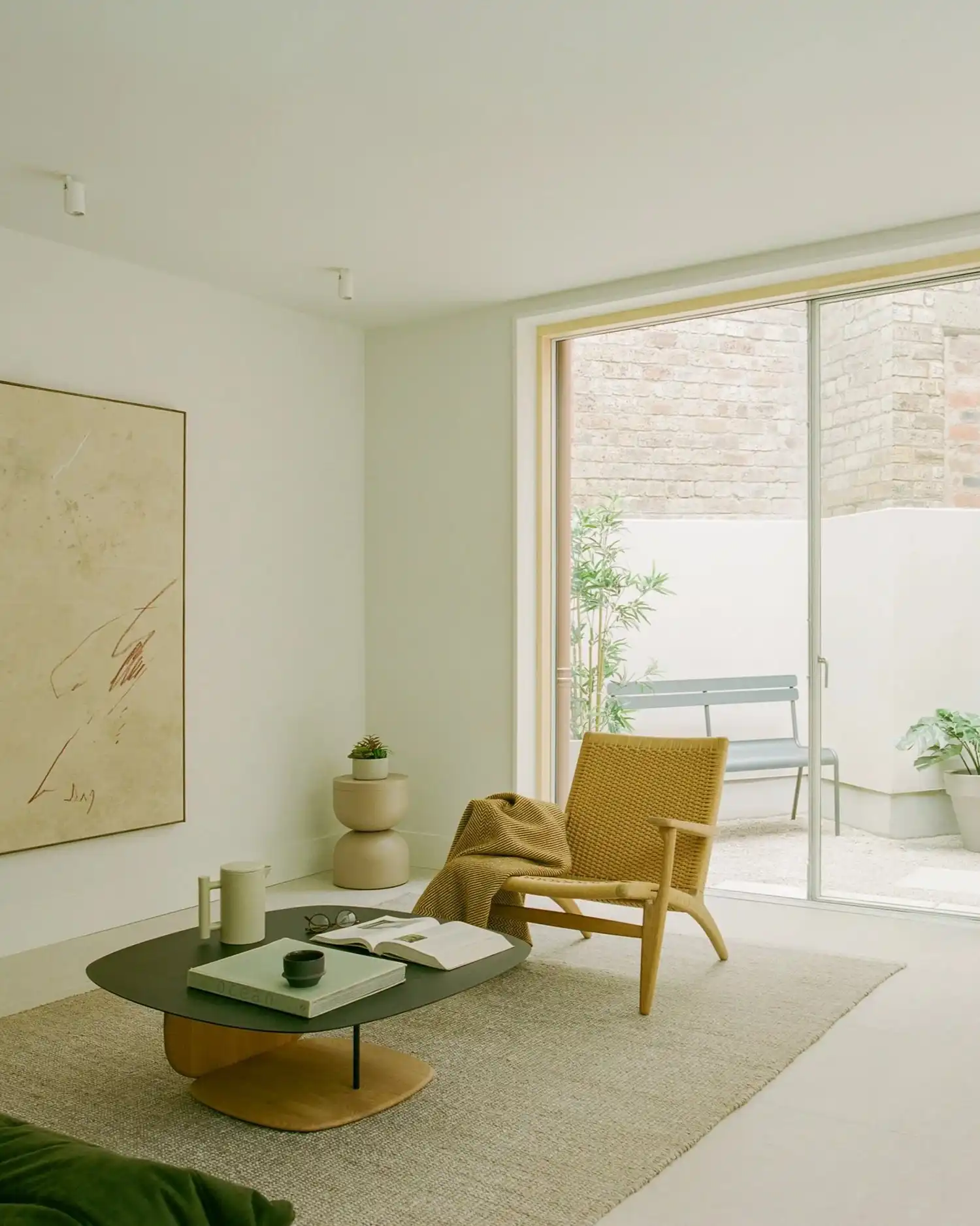 Living room with a woven lounge chair, olive coffee table, and large window to a courtyard.