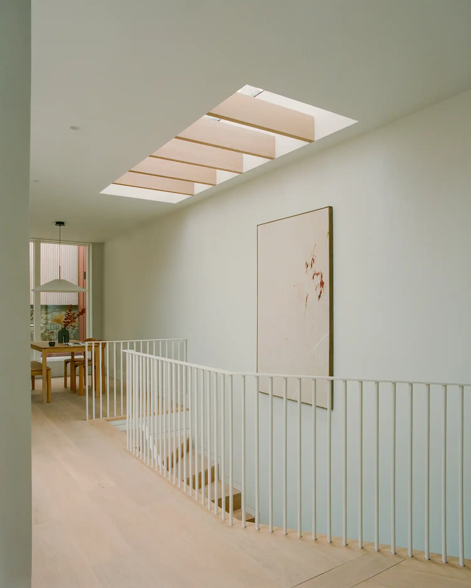 White hallway with a minimalist metal balustrade and a large rectangular skylight above.