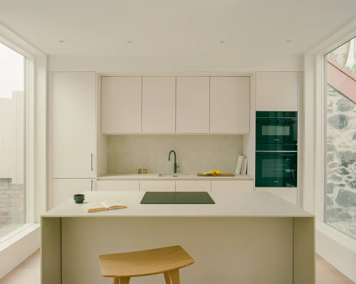 Modern white kitchen with a central island and floor-to-ceiling windows on both sides.