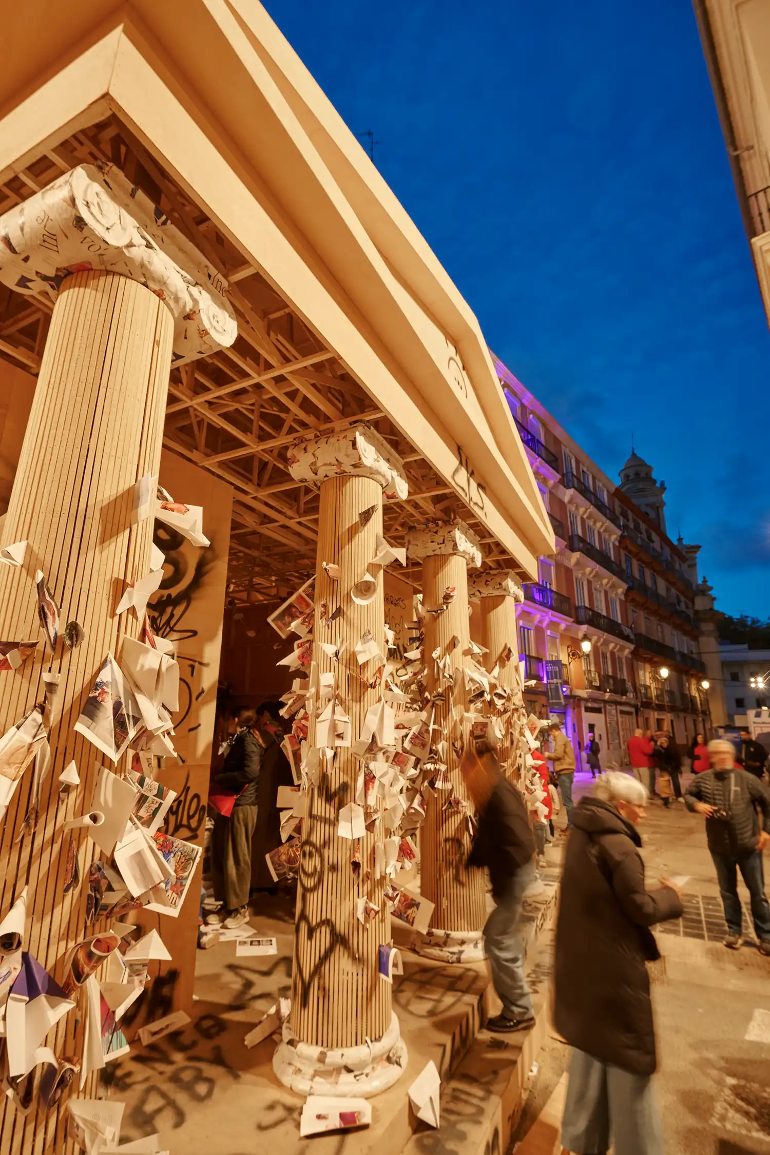 Detailed view of the Ionic columns covered in paper offerings and graffiti at night.